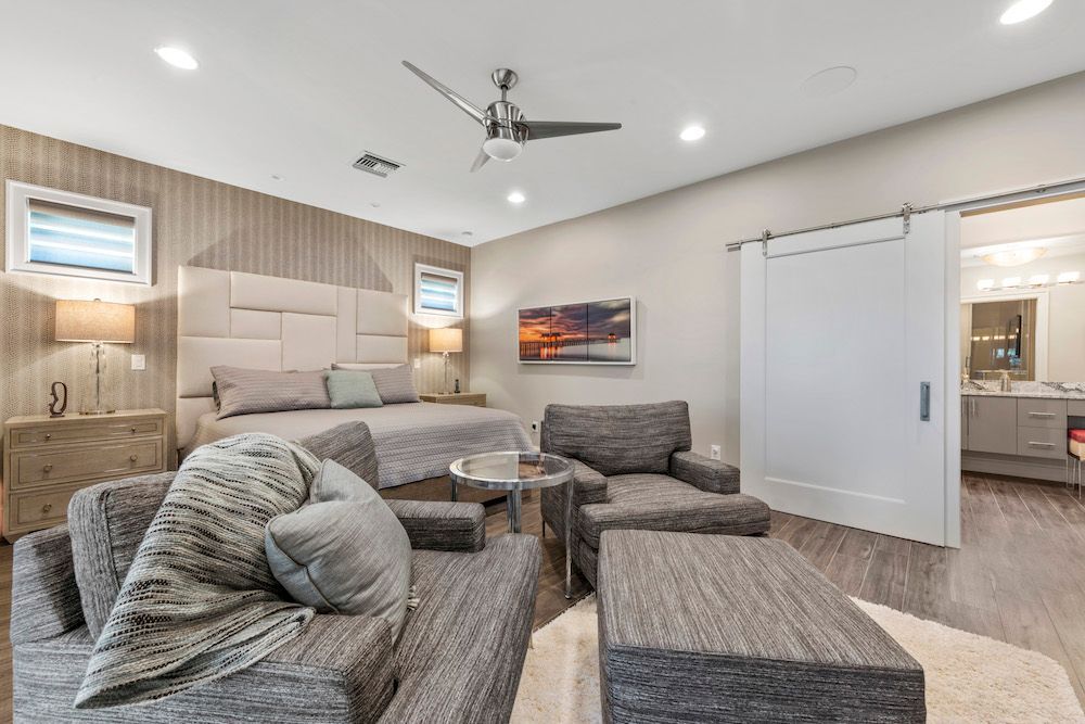 A bedroom with a couch , chair , table and ceiling fan.