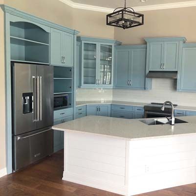 A kitchen with blue cabinets , a stainless steel refrigerator , a sink , and a large island.
