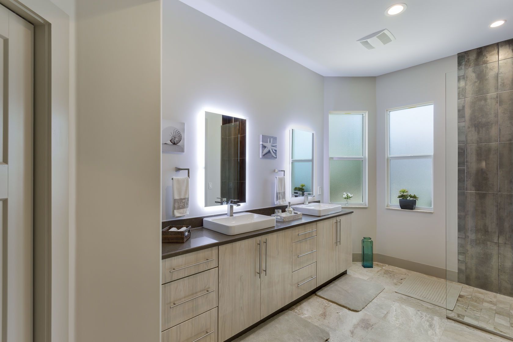A bathroom with two sinks , two mirrors and a walk in shower.