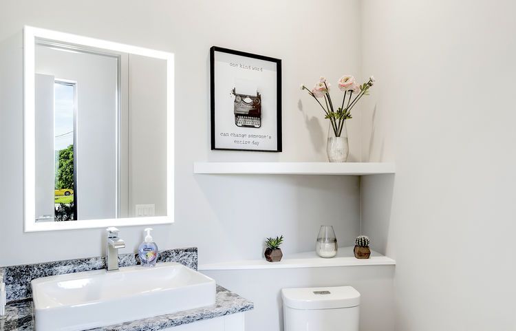 A bathroom with a sink , toilet , mirror and shelf.