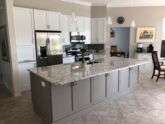 A kitchen with white cabinets , granite counter tops , stainless steel appliances and a large island.