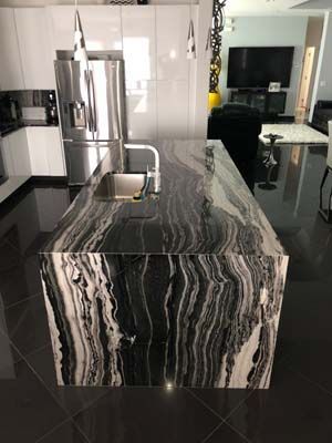 A kitchen with a black and white granite counter top and a stainless steel refrigerator.