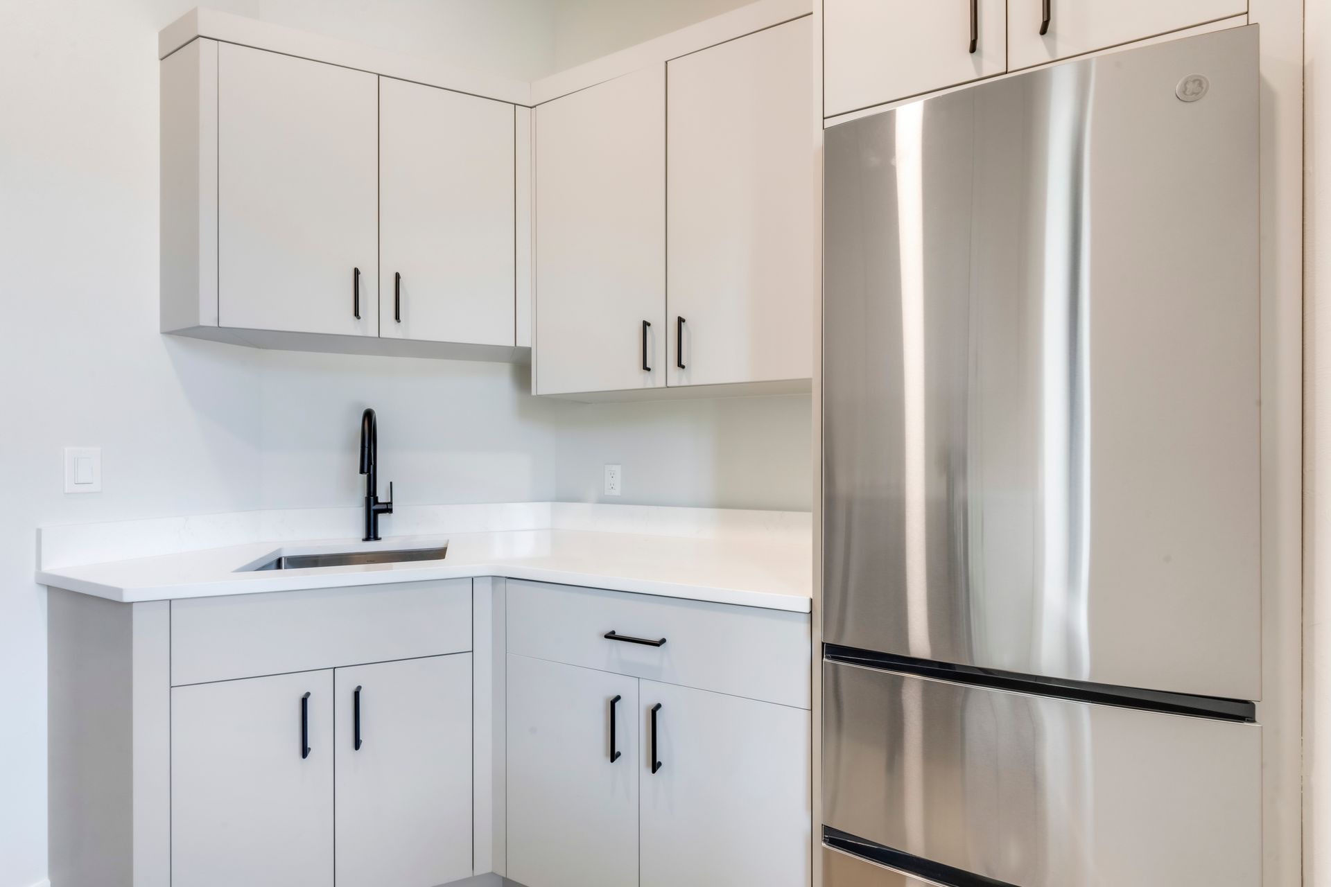 A kitchen with white cabinets and a stainless steel refrigerator.