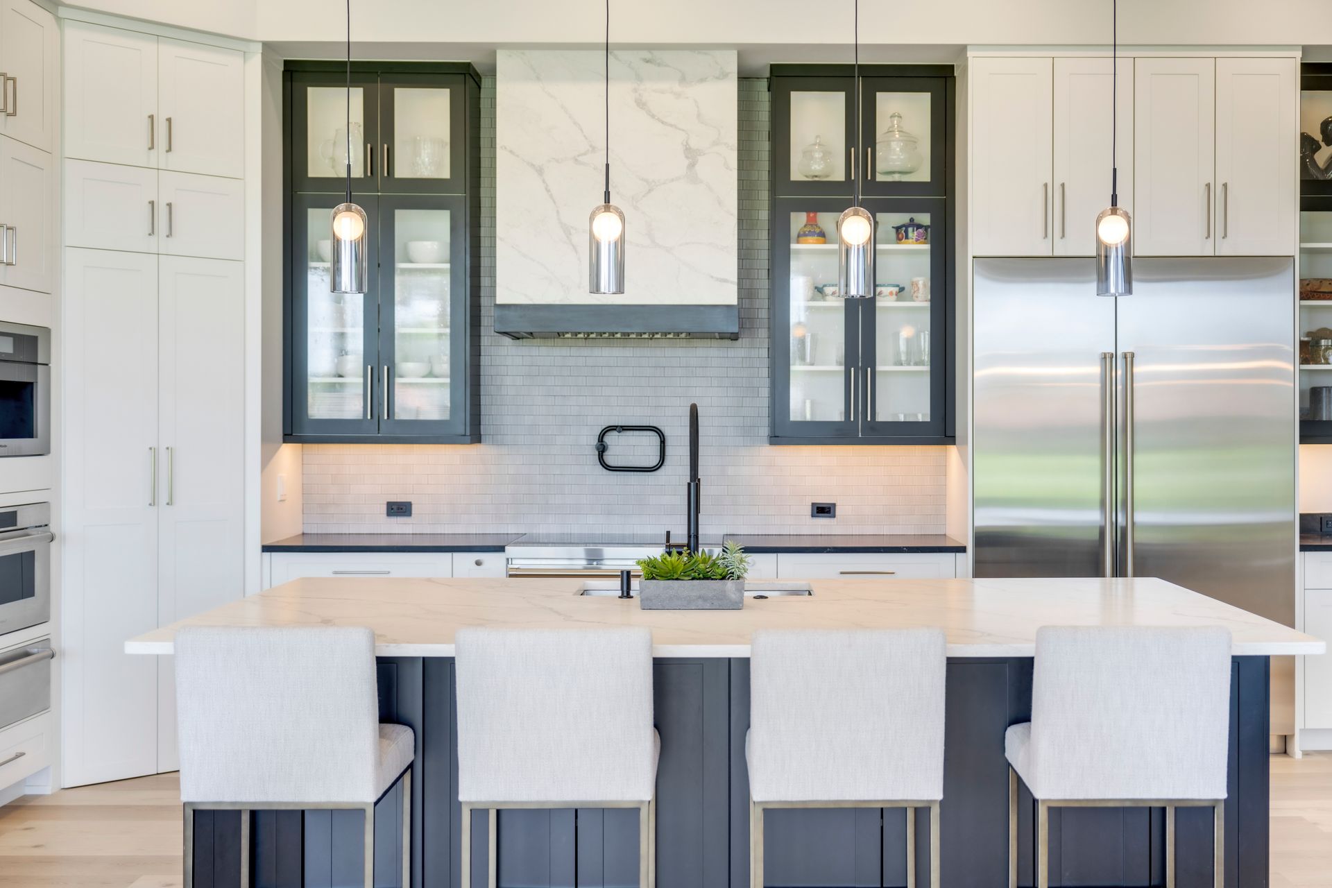A kitchen with white cabinets , stainless steel appliances , a large island and chairs.