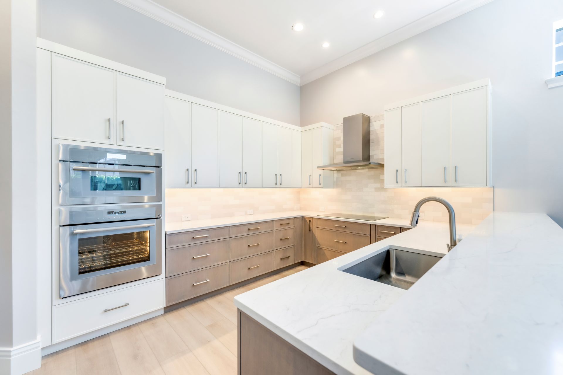 A kitchen with white cabinets , stainless steel appliances , a sink , and an oven.