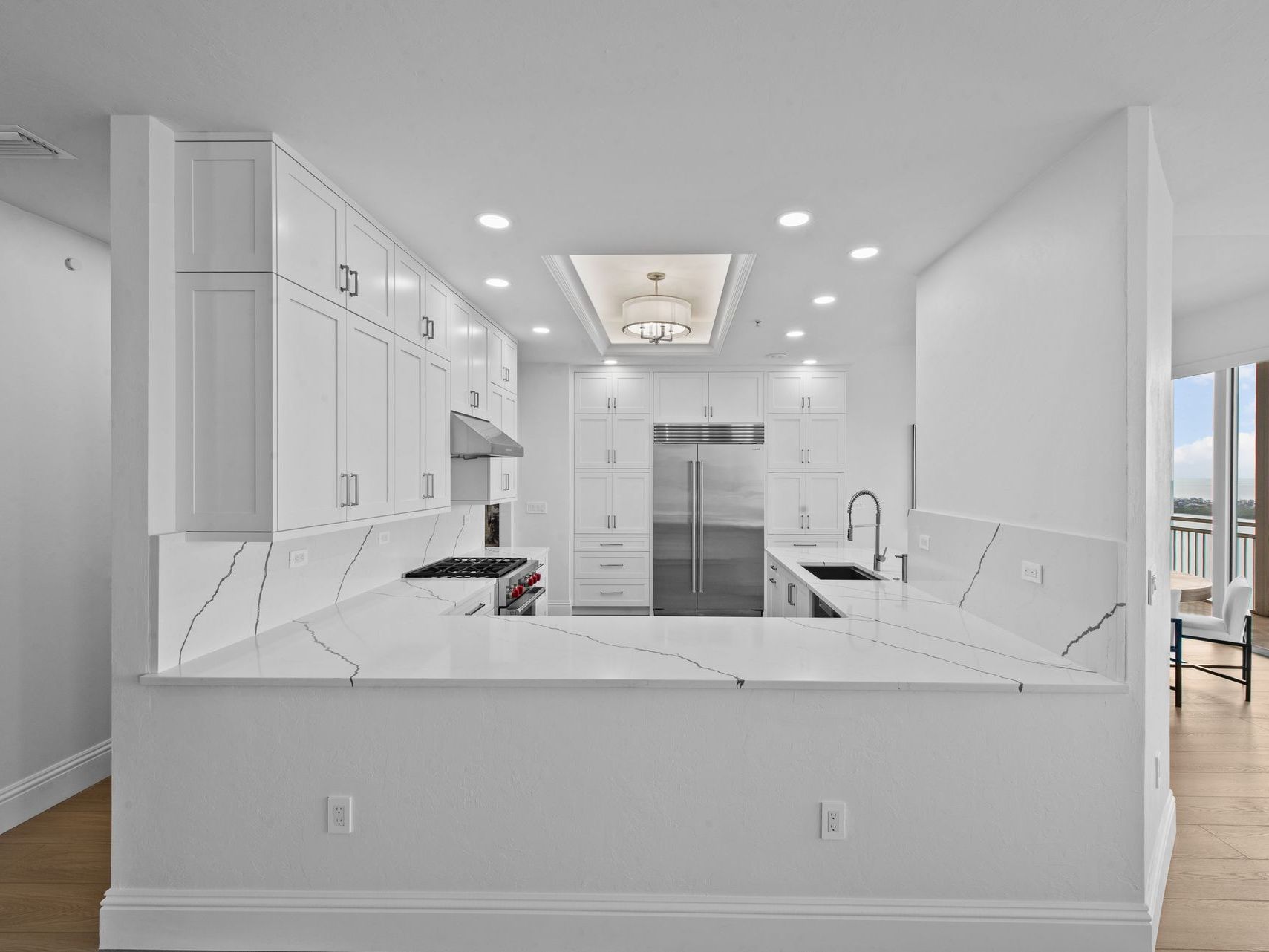 A kitchen with white cabinets , white counter tops , a refrigerator and a sink.