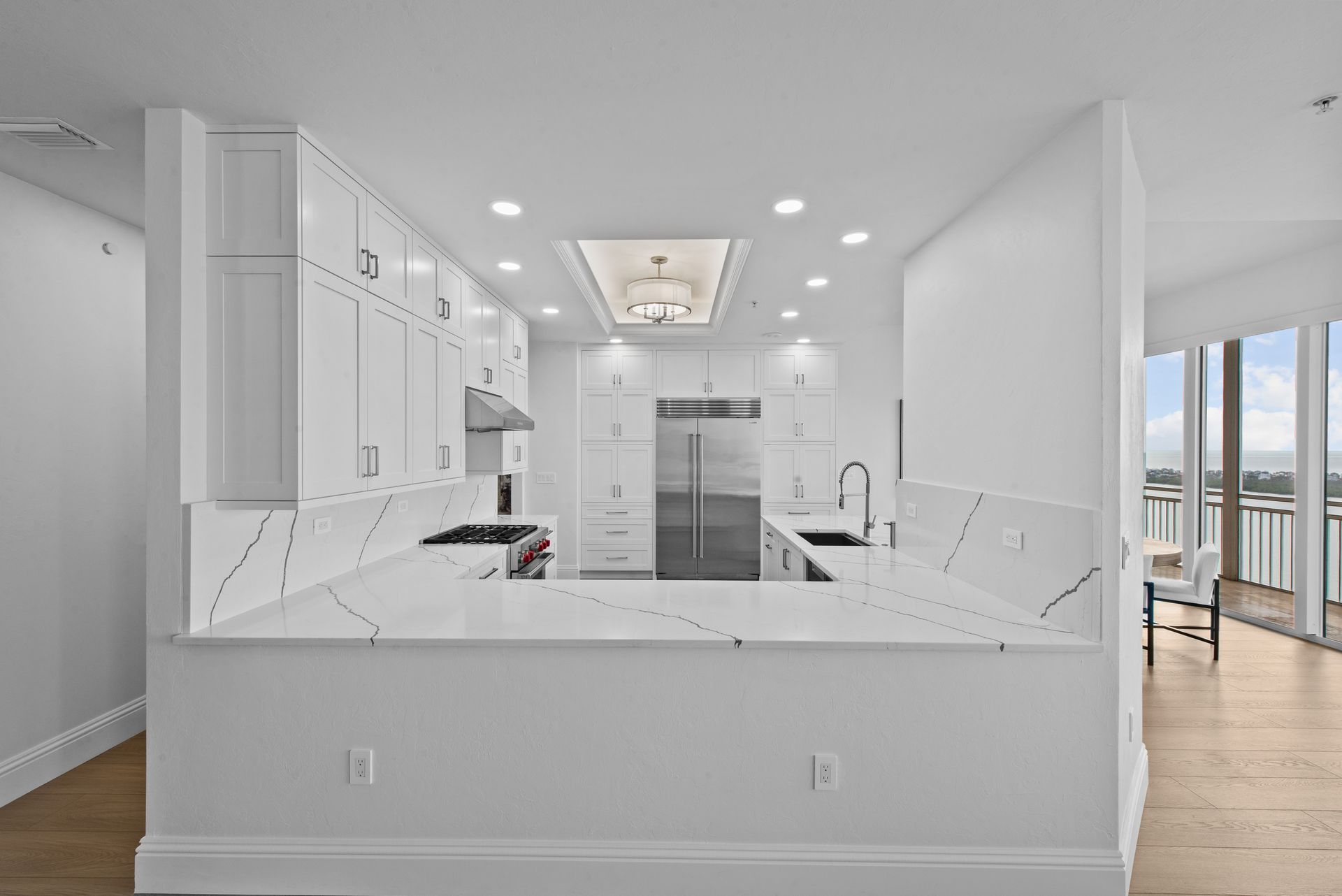 A kitchen with white cabinets , granite counter tops , stainless steel appliances and a large window.