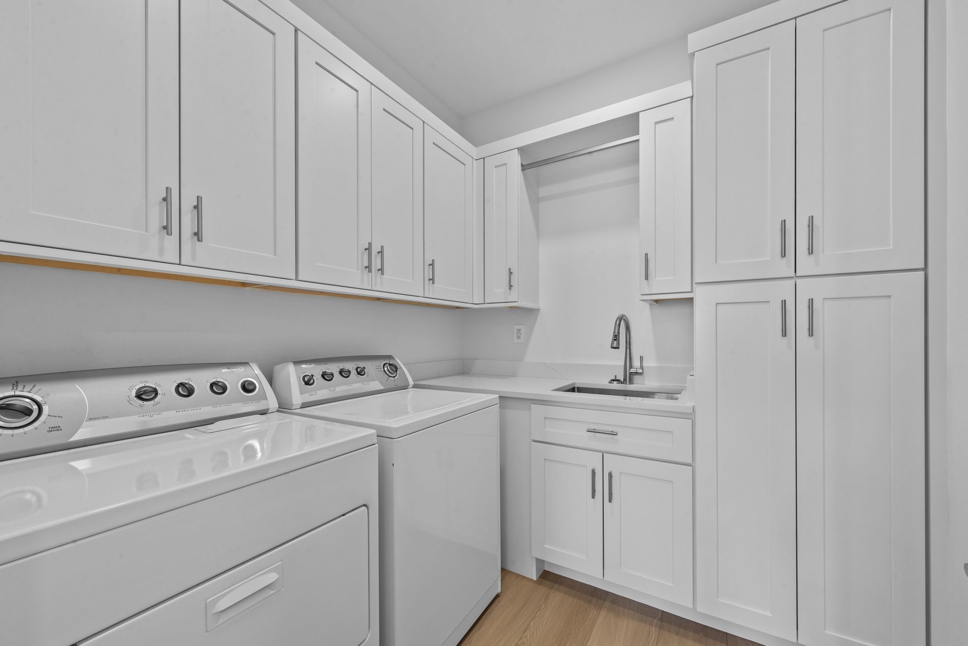 A laundry room with white cabinets , a washer and dryer , and a sink.