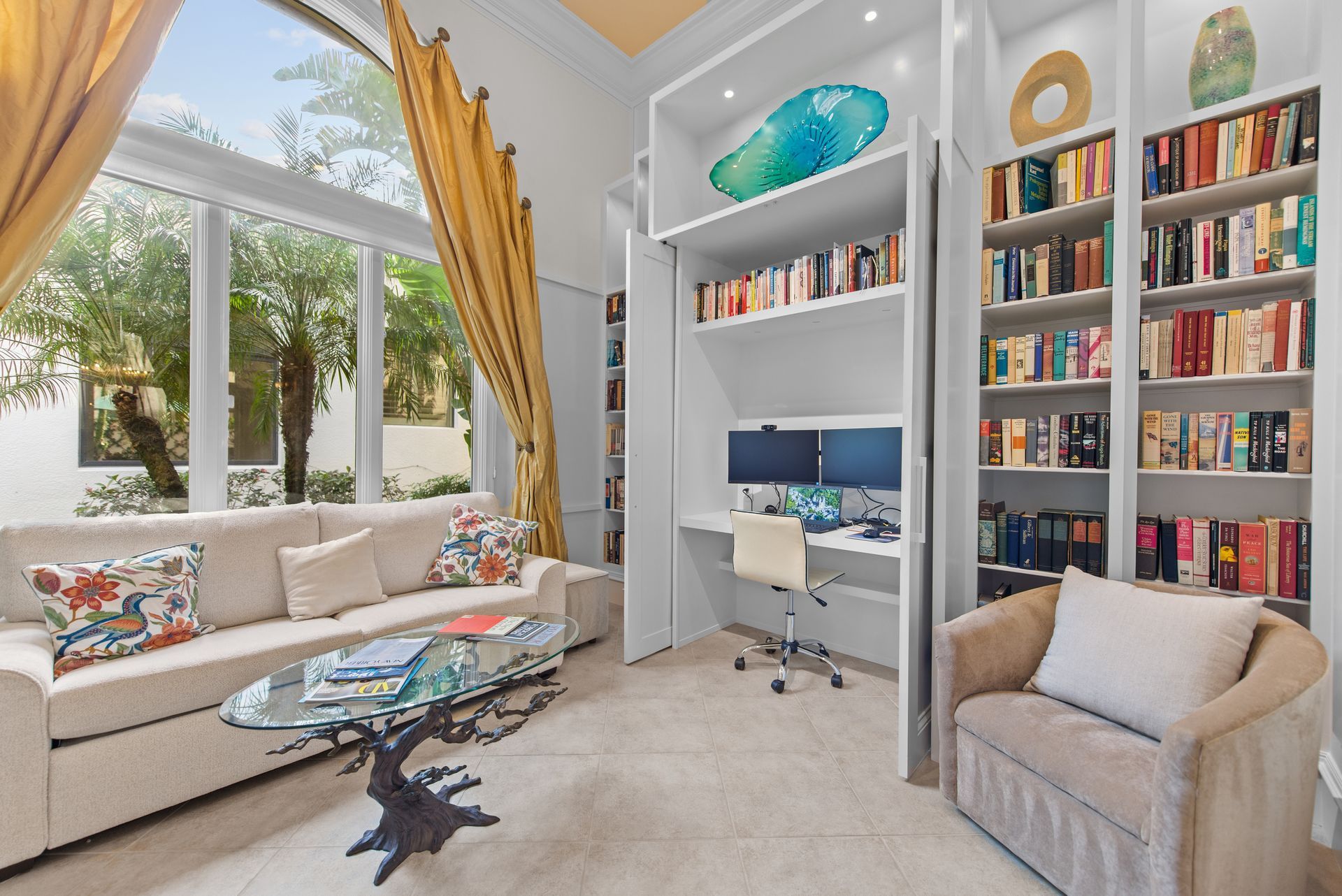 A living room with a couch , chair , desk and shelves filled with books.