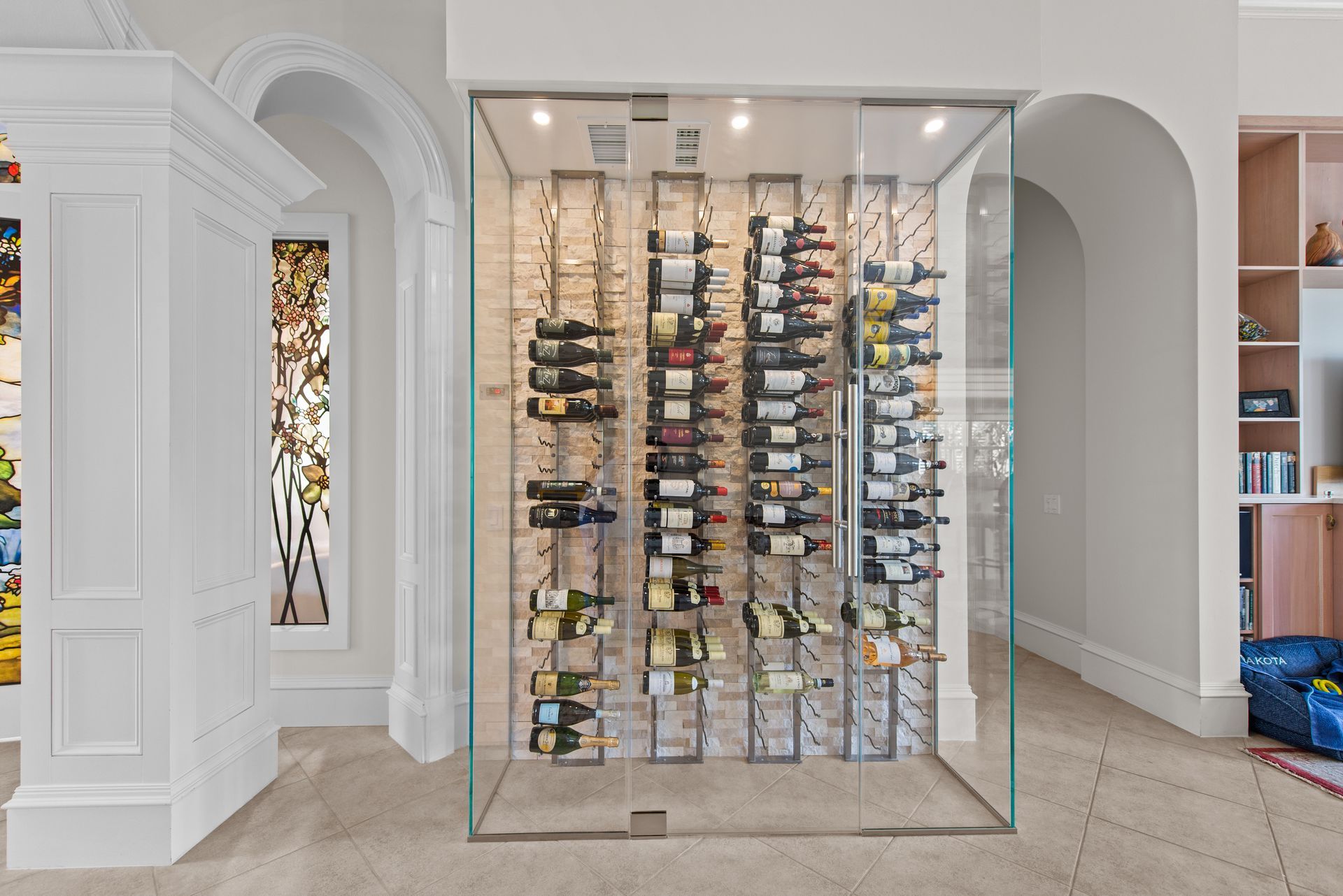 A glass wall filled with bottles of wine in a room.