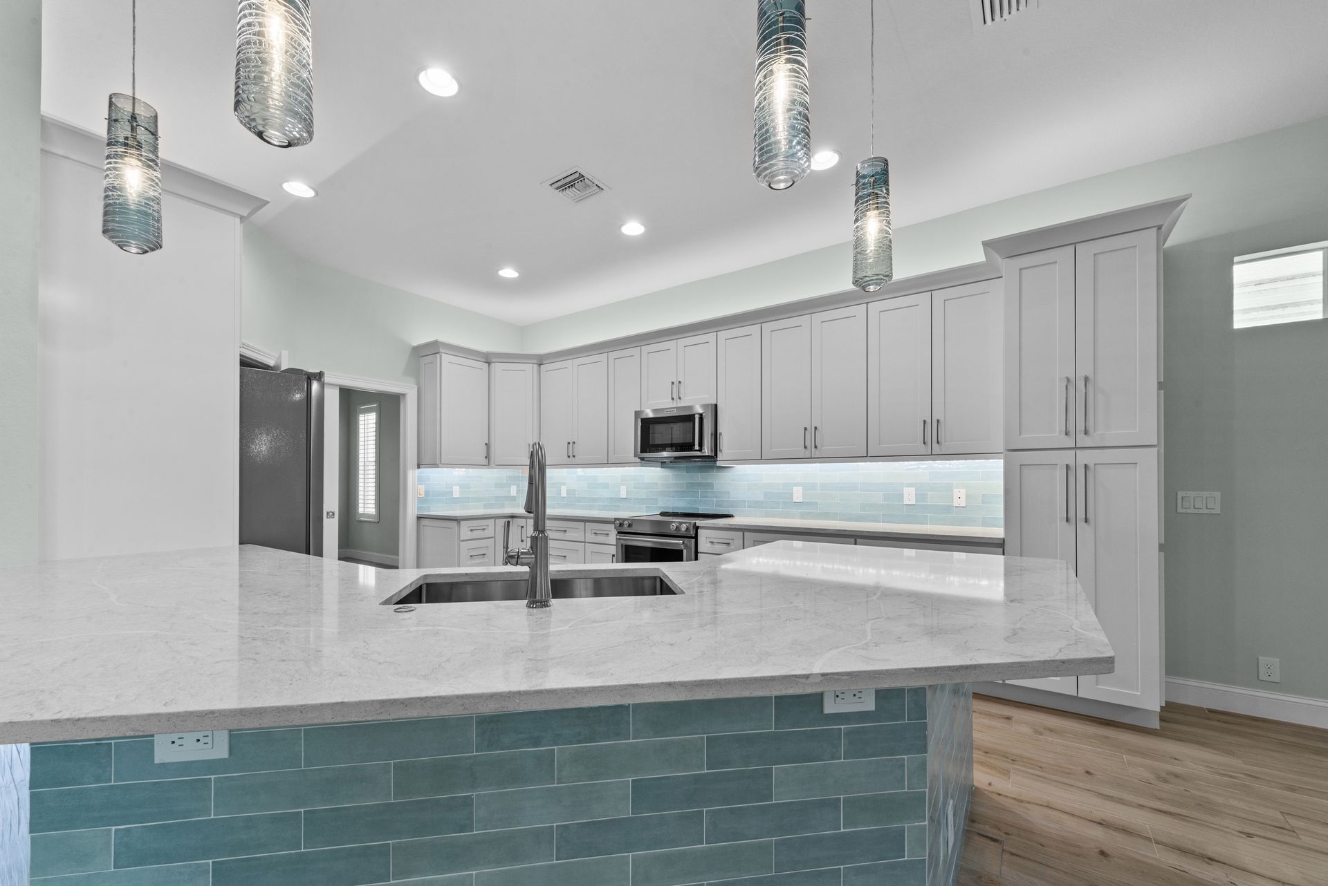 A kitchen with white cabinets and blue tiles and a large island.