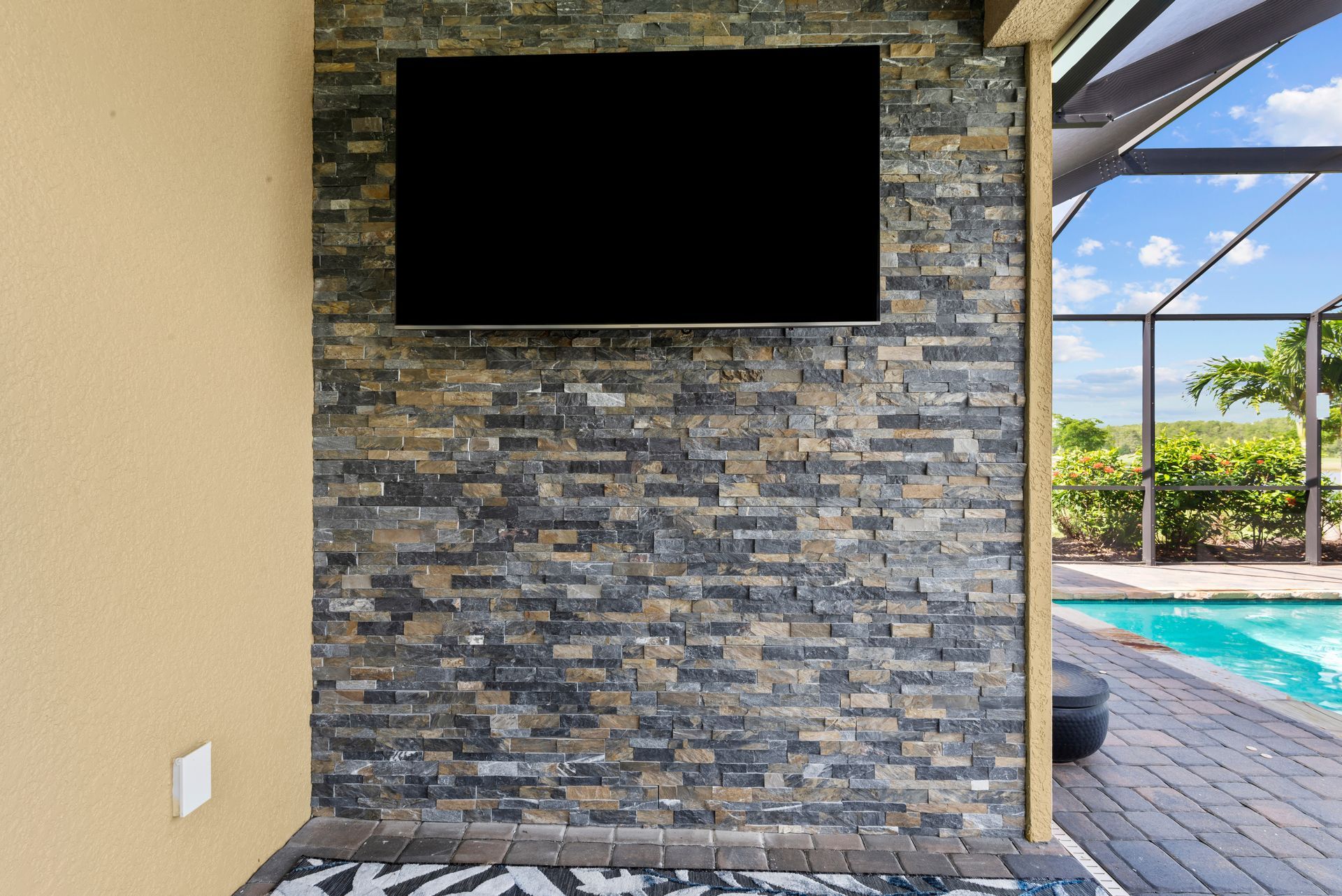 A television mounted on a stone wall next to a pool.