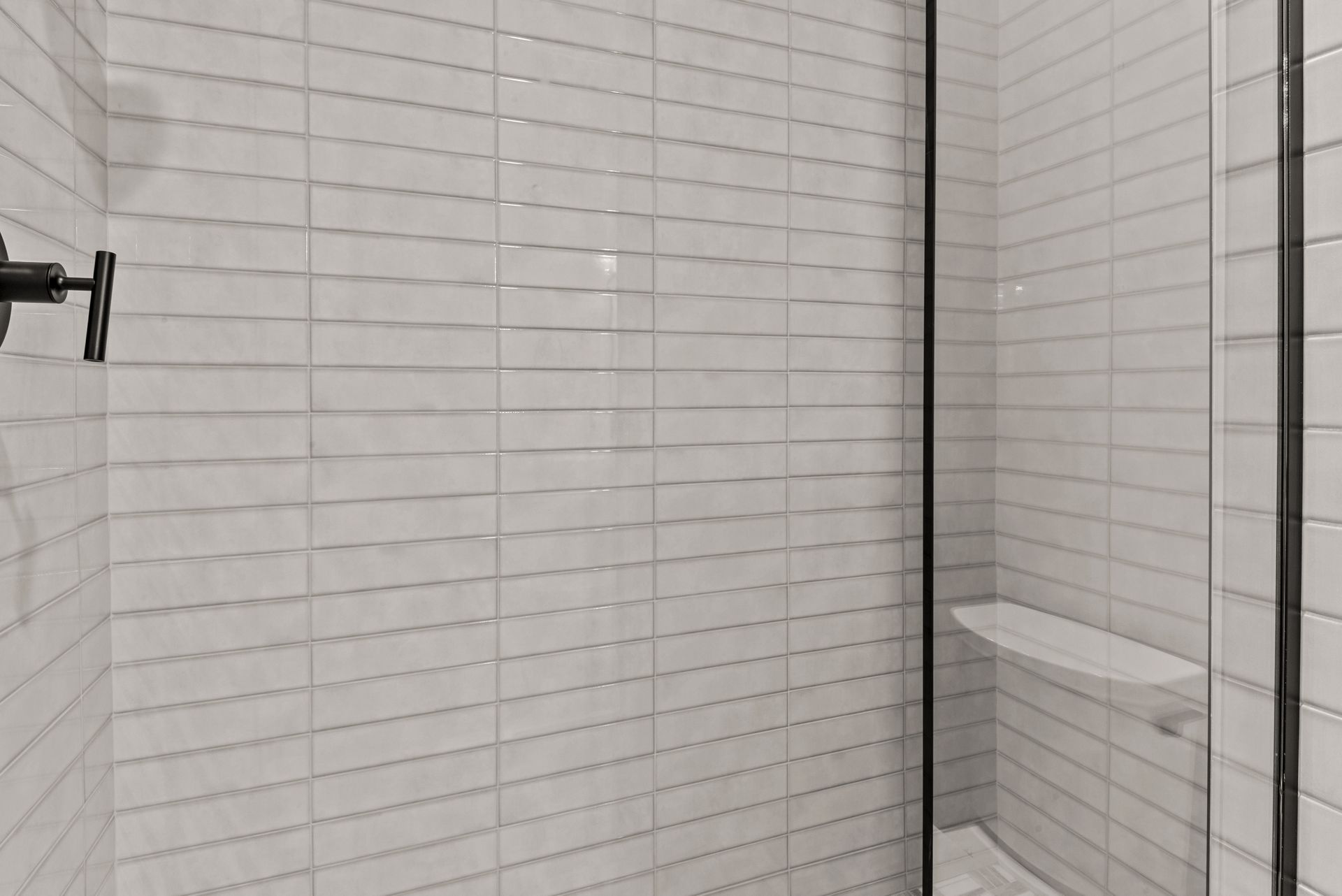A bathroom with white tiles and a walk in shower with a glass door.