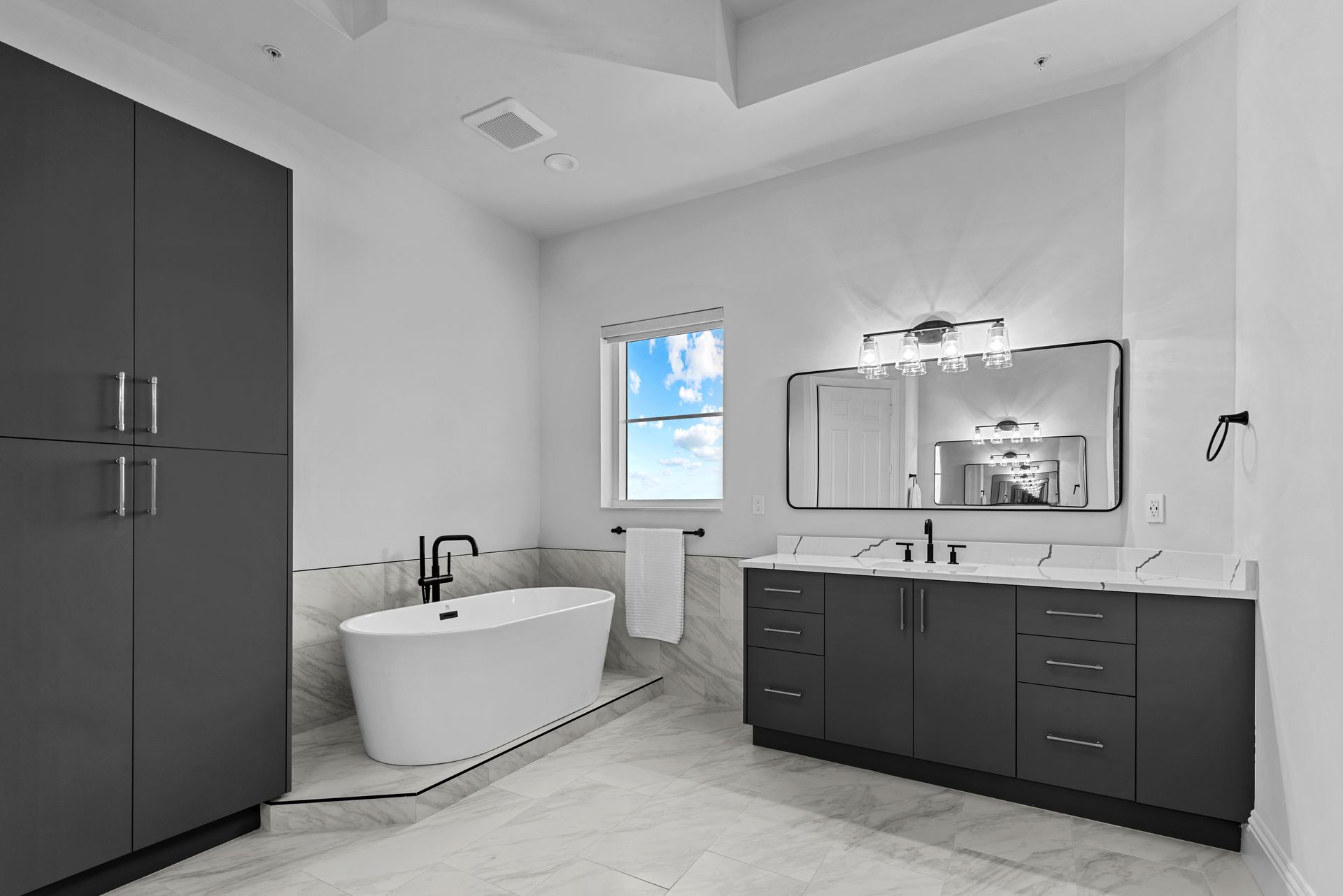A bathroom with a tub , sink , mirror and cabinets.