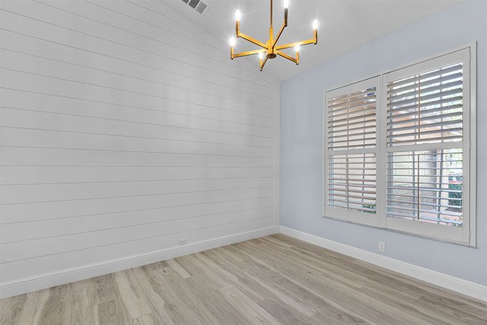 An empty room with a chandelier and shutters on the windows.