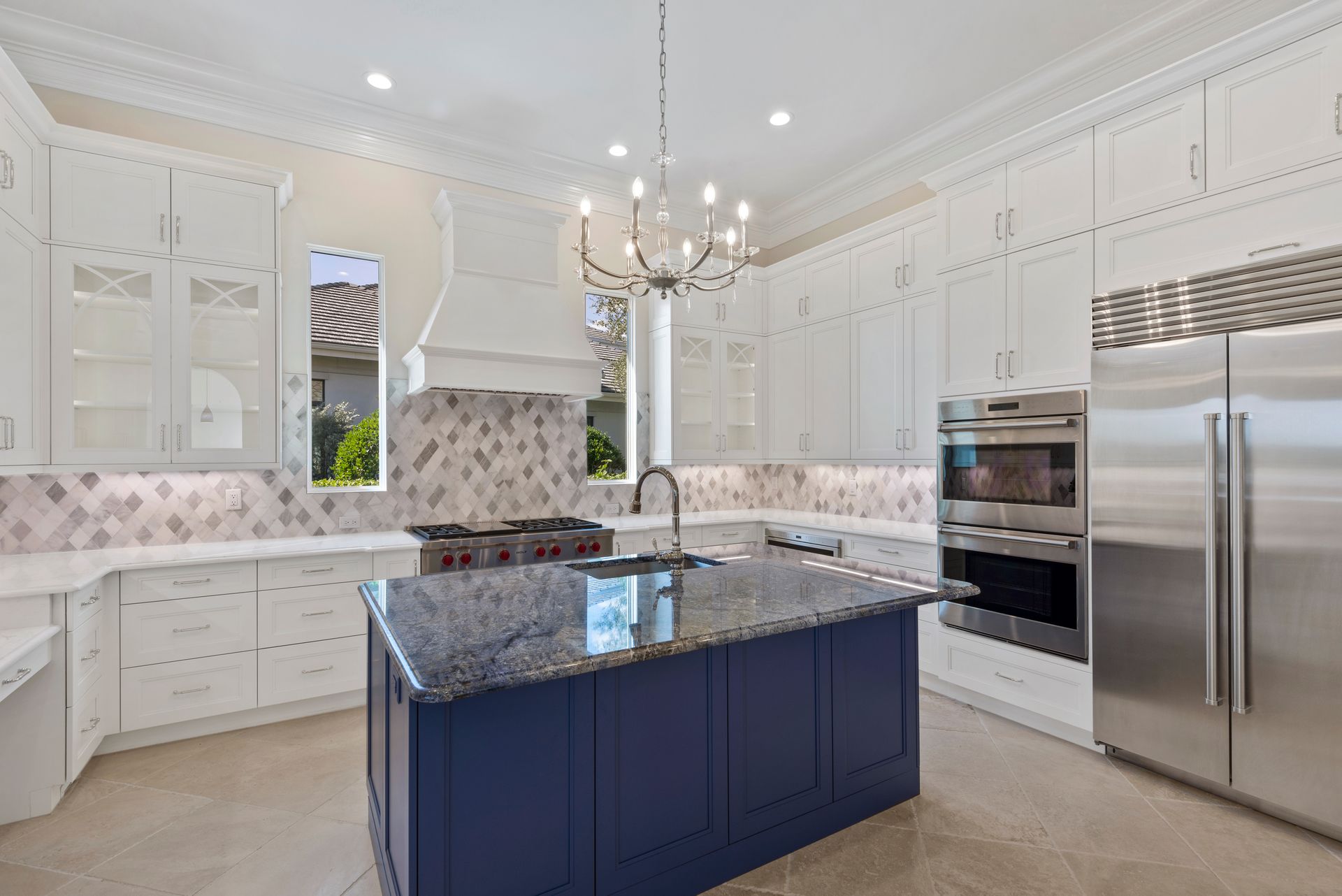 A kitchen with white cabinets , stainless steel appliances , a blue island , and a chandelier.