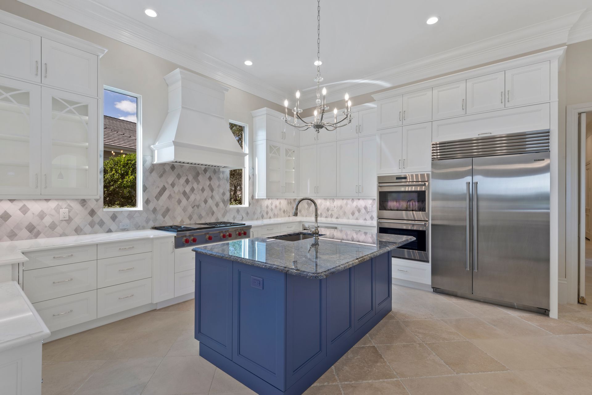A kitchen with white cabinets , stainless steel appliances , and a blue island.