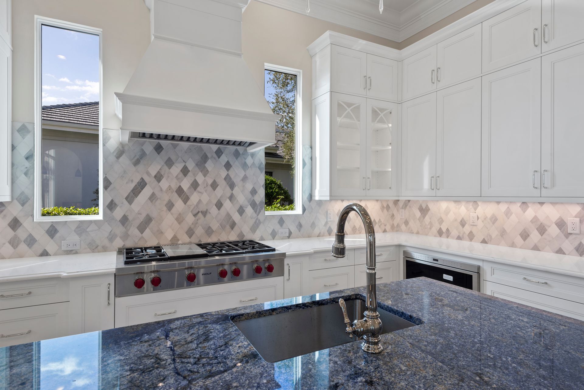 A kitchen with granite counter tops , white cabinets , a stove and a sink.