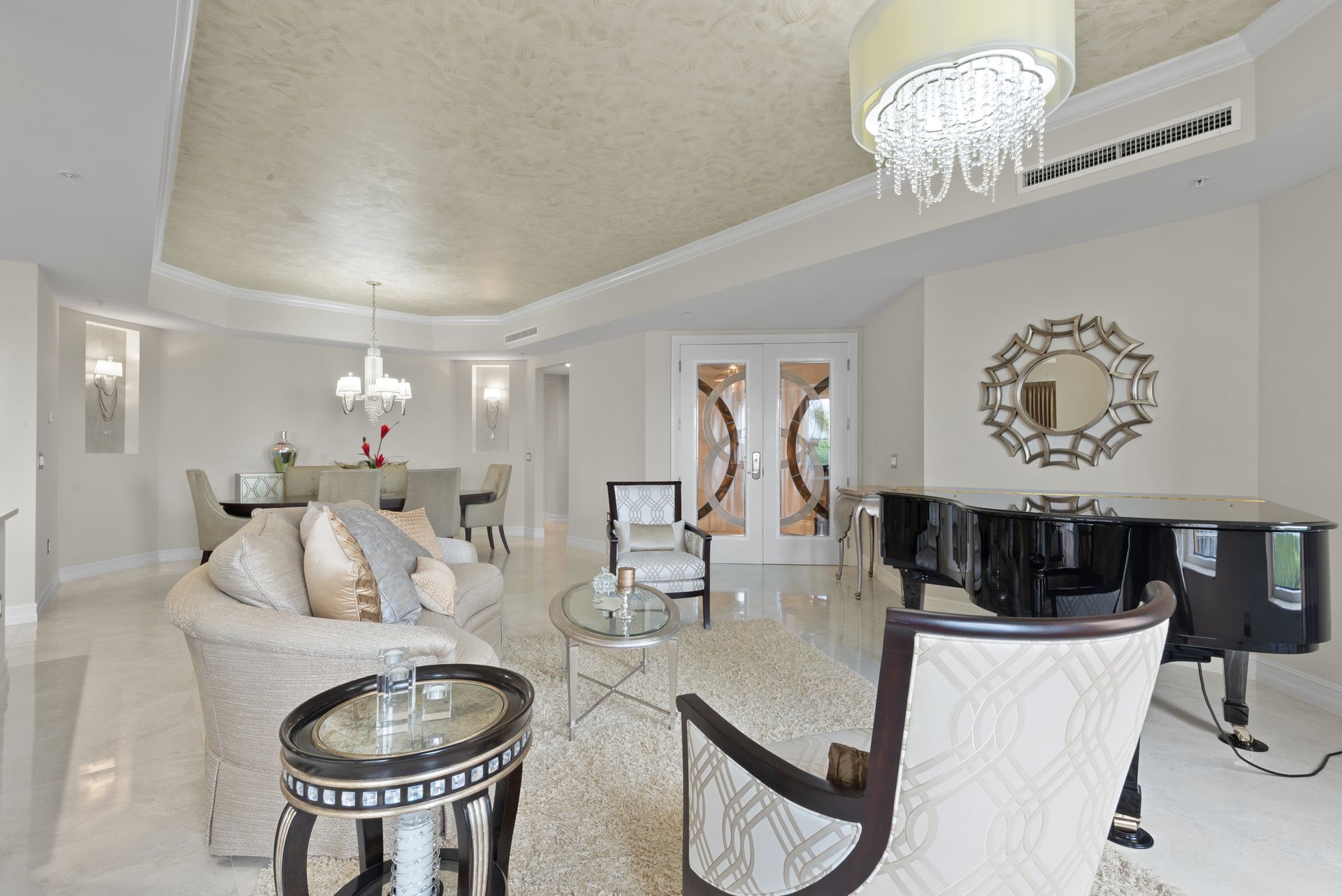 A living room with a piano , chairs , tables and a chandelier.