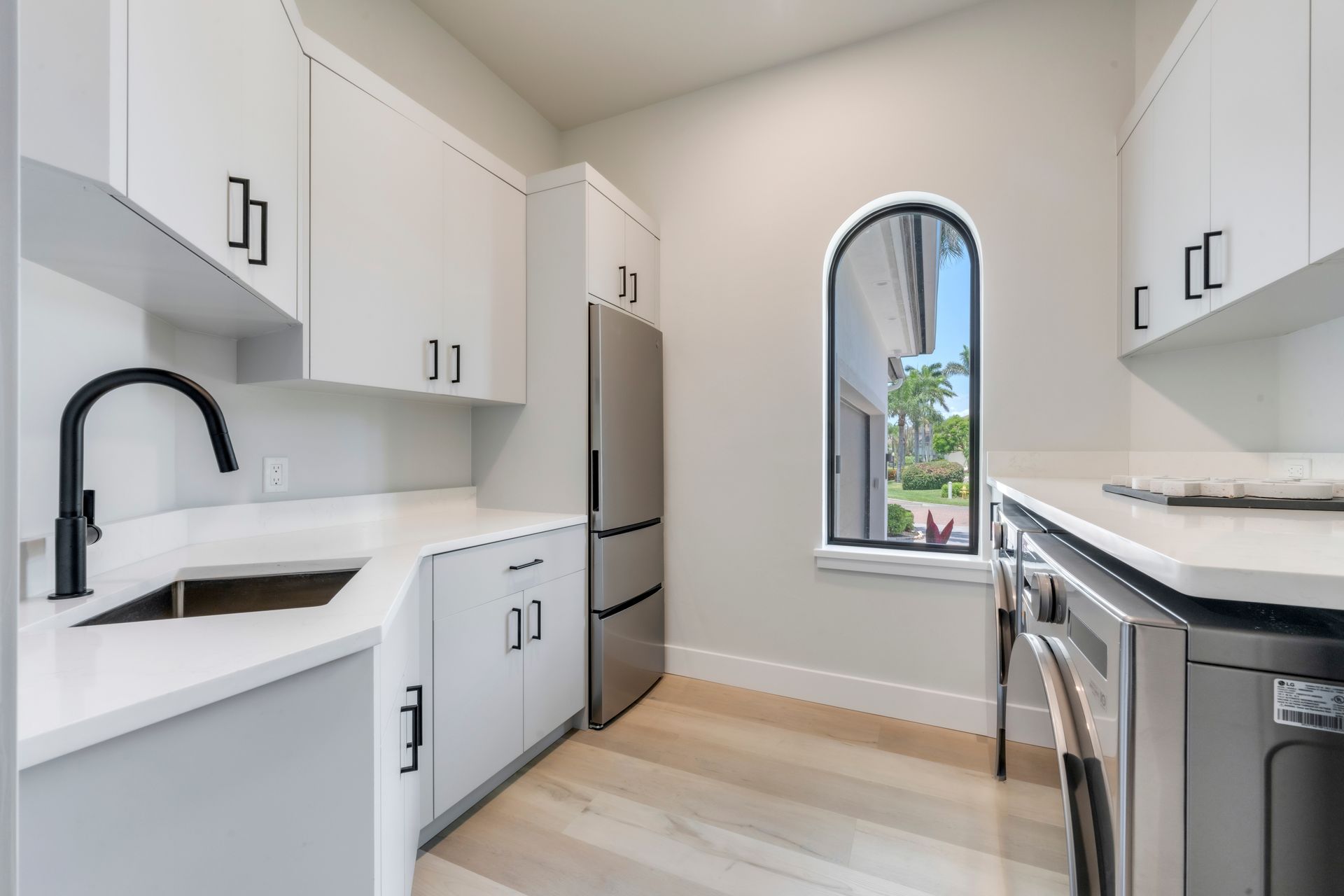 A kitchen with white cabinets , stainless steel appliances , a sink and a window.
