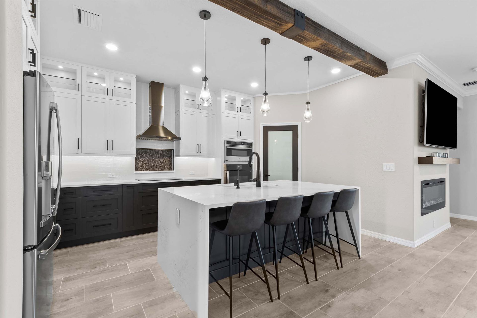 A kitchen with a large island , stools , a refrigerator and a television.
