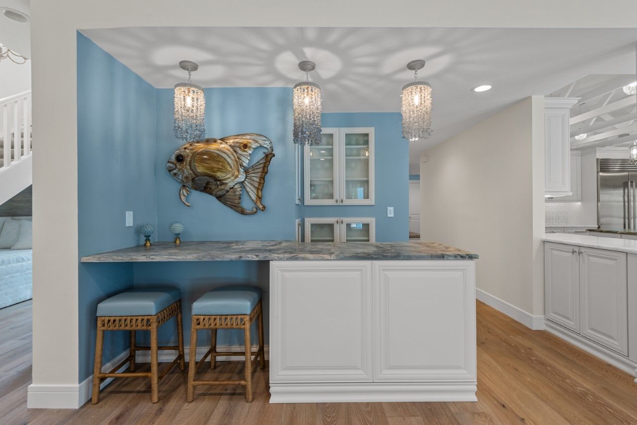 A kitchen with blue walls and white cabinets and a bar with stools.