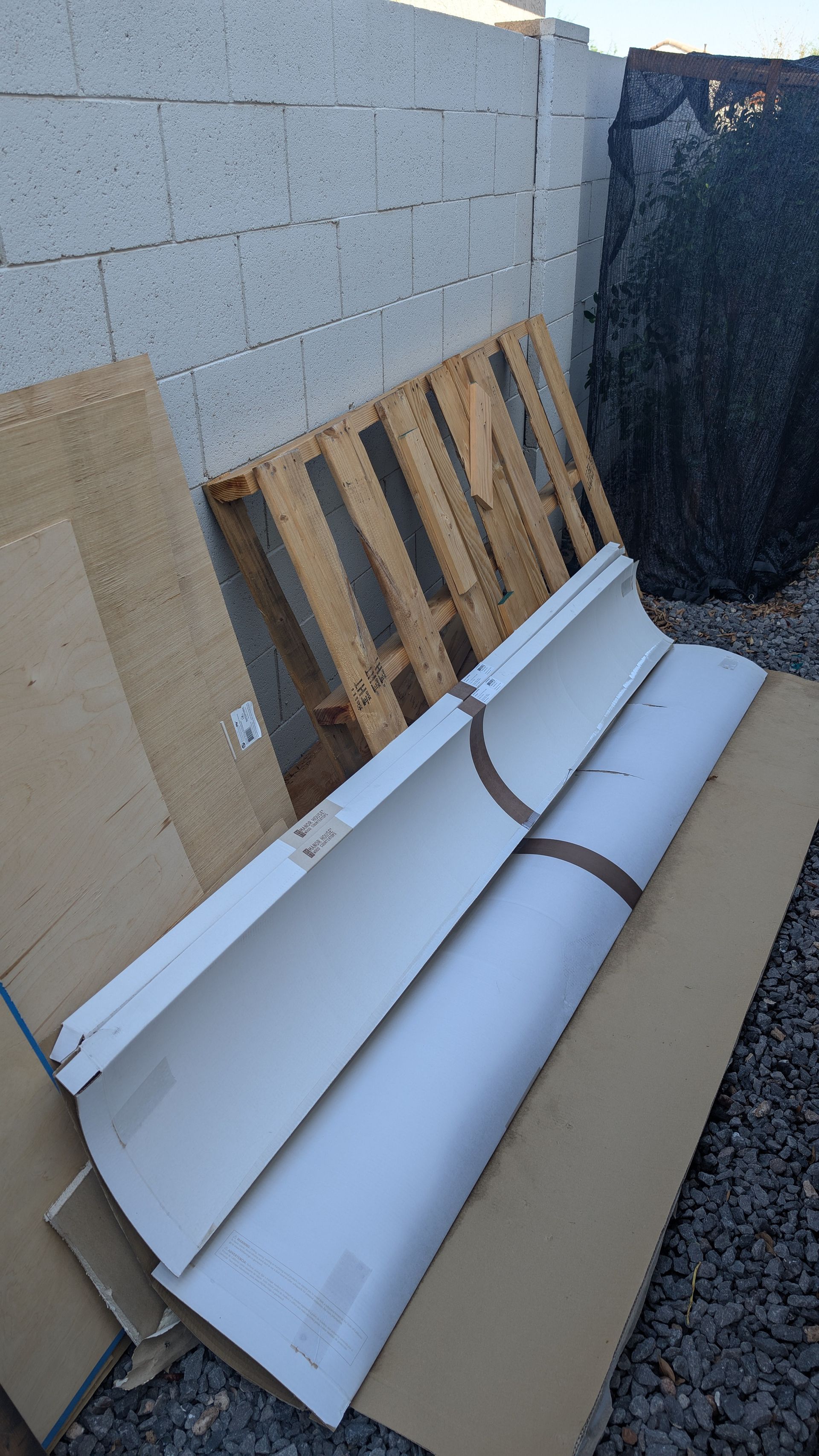 Two silver car panels and a wooden pallet lean against a cinder block wall.