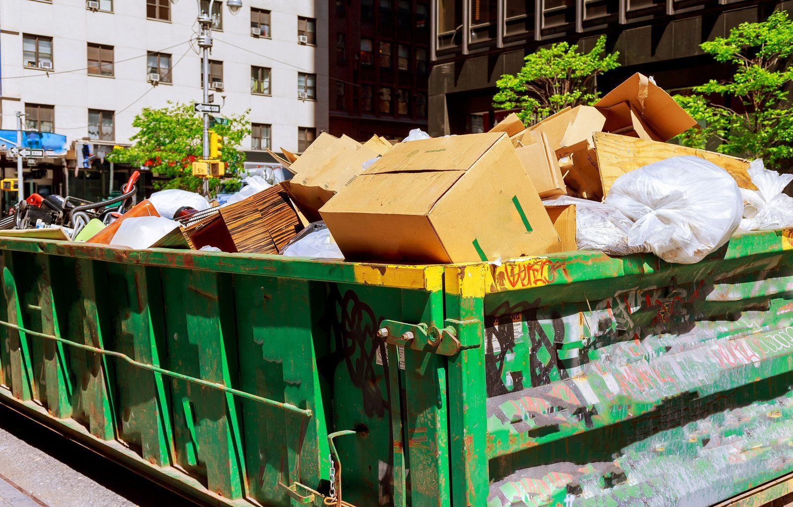 A green dumpster filled with cardboard boxes and plastic bags.