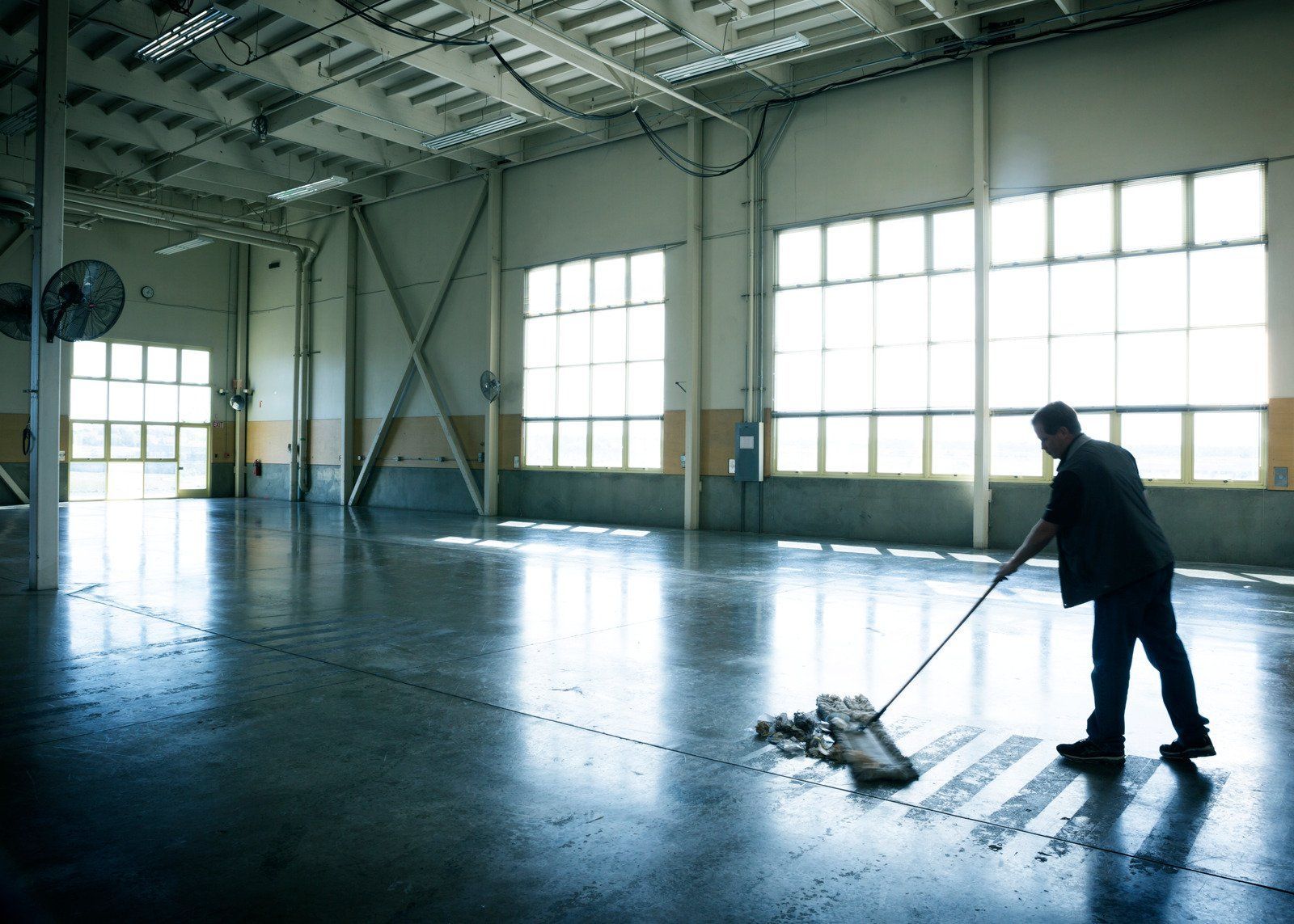 A man is mopping the floor of a large warehouse.