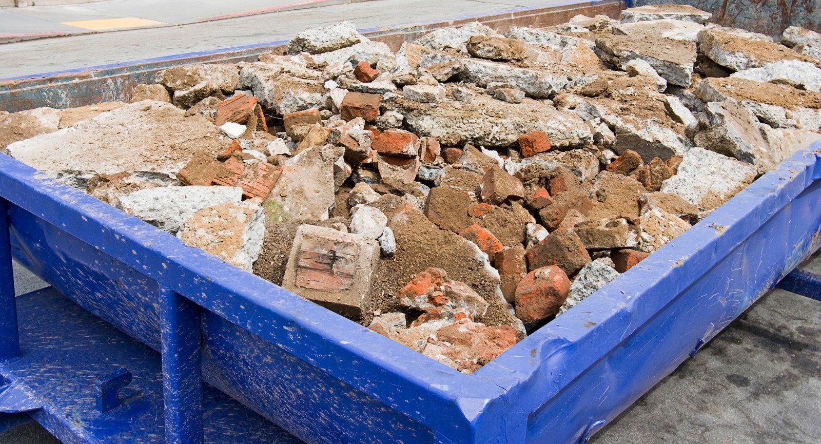 A blue dumpster filled with bricks and concrete.