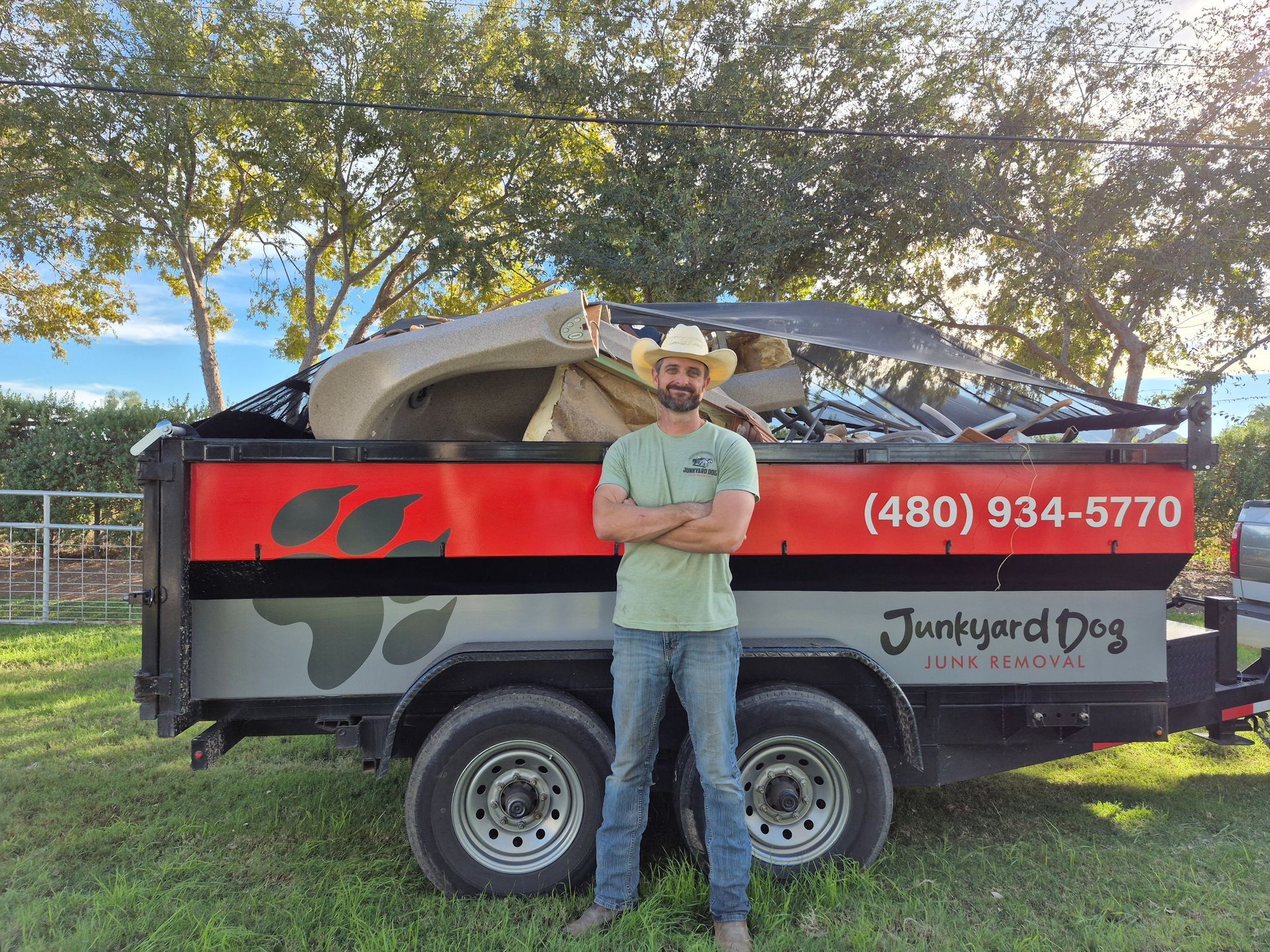 Man in cowboy hat stands by a trailer filled with junk. Trailer has 