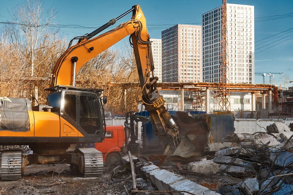 A yellow excavator is destroying a building on a construction site.