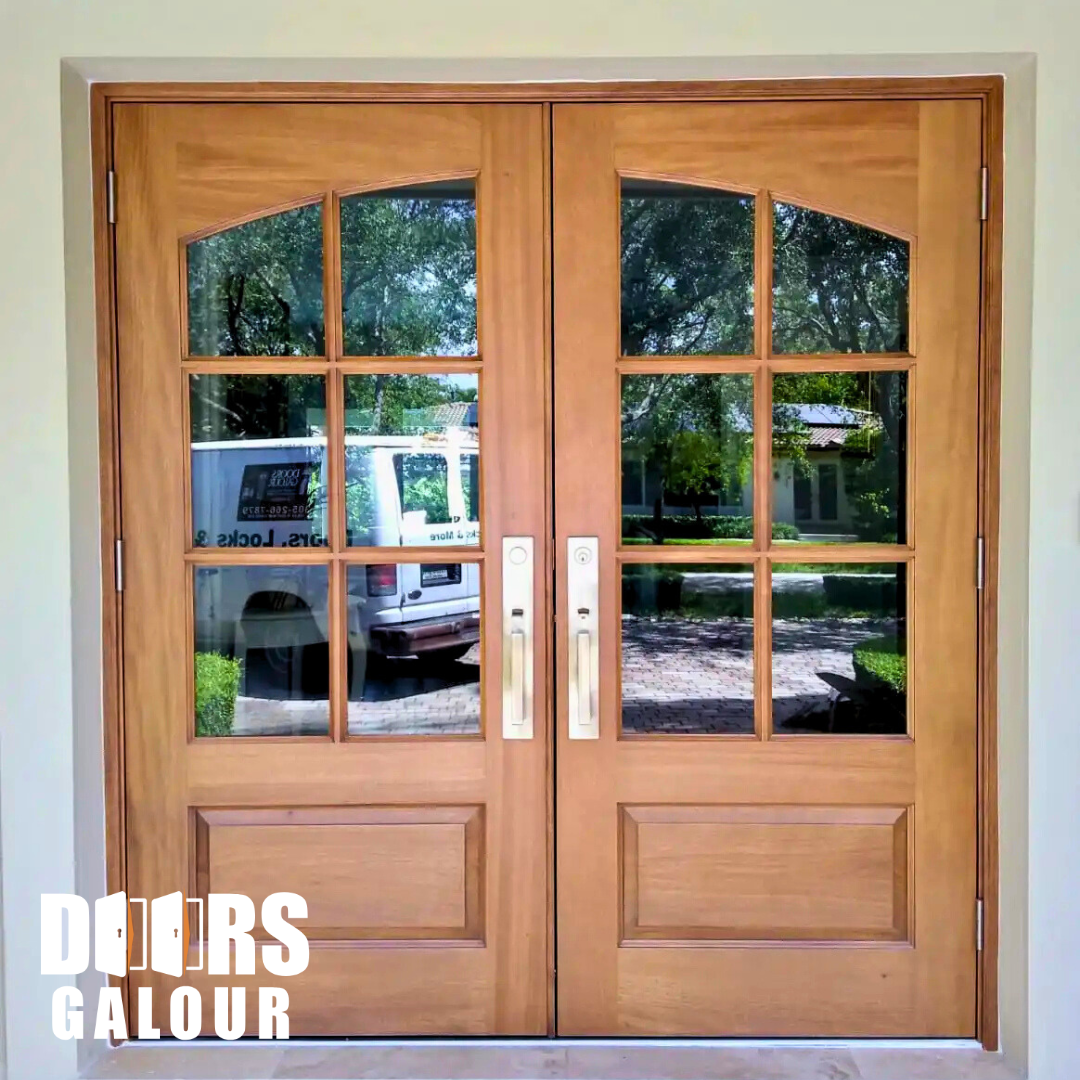 Wooden double doors with glass panes reflecting a vehicle and trees; brass handles, light-colored trim.