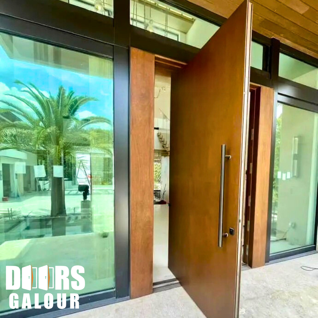 Wooden front door, ajar, with a modern design, between glass windows; tropical setting.