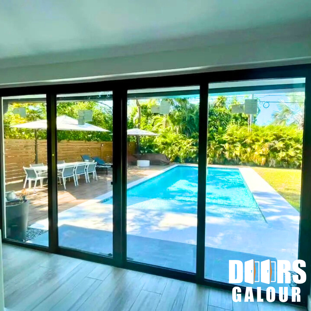 Sliding glass doors open to a pool and outdoor dining area. Black frames, green trees, blue water, and sunlight.