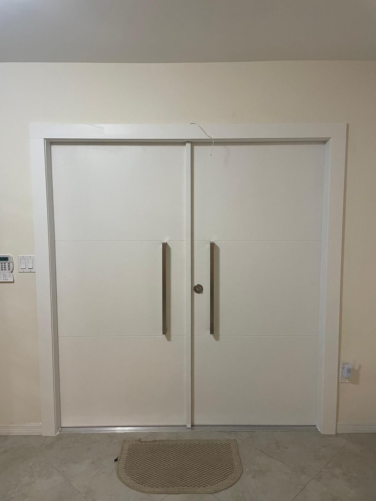 White double doors with silver handles and a small welcome mat.