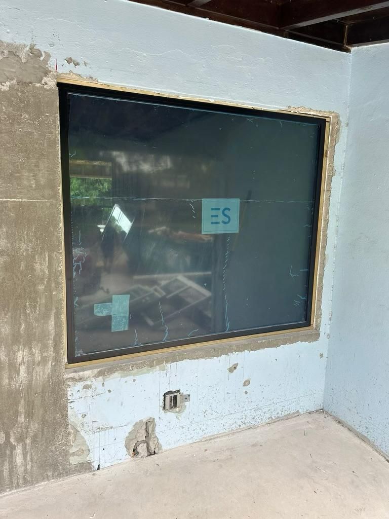 Newly installed window in a concrete wall, with unfinished stucco surrounding it.