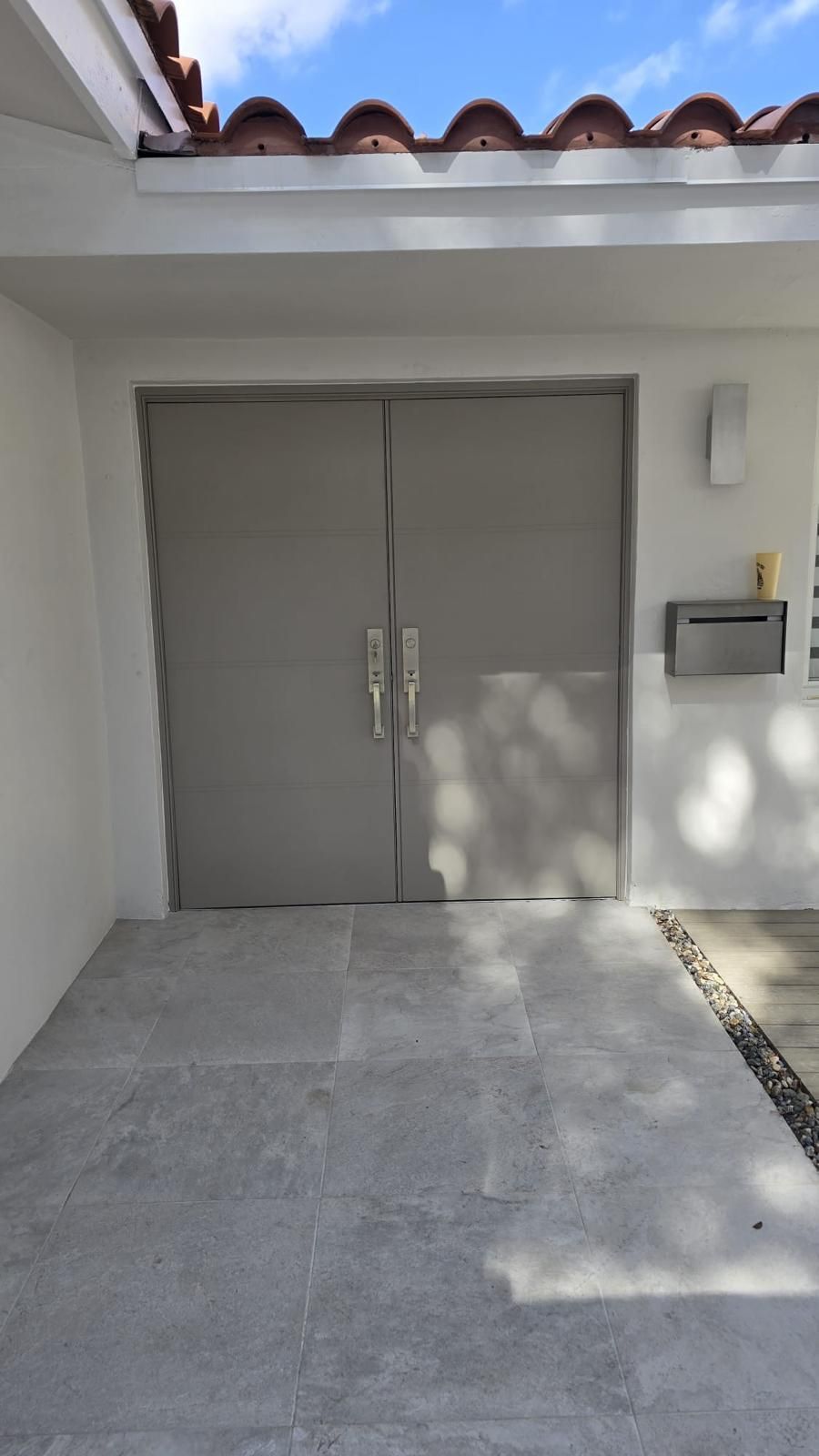 Gray double Fiberglass doors on a house with a tiled entrance and a mailbox.