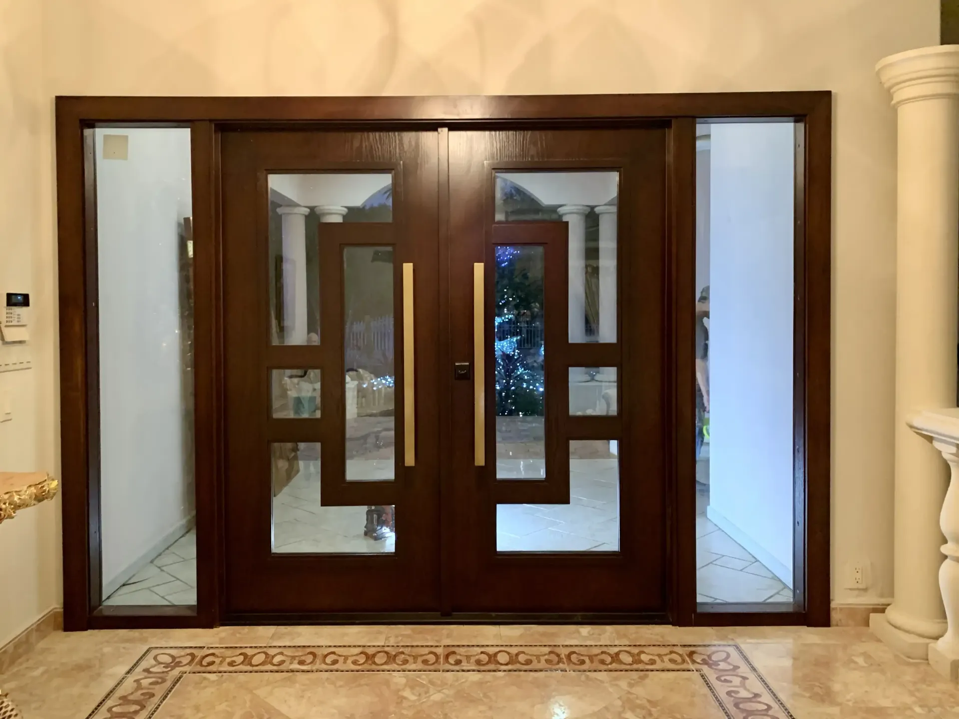 Dark wood double front doors in South Florida with glass panels, sidelights, and a gold handle.