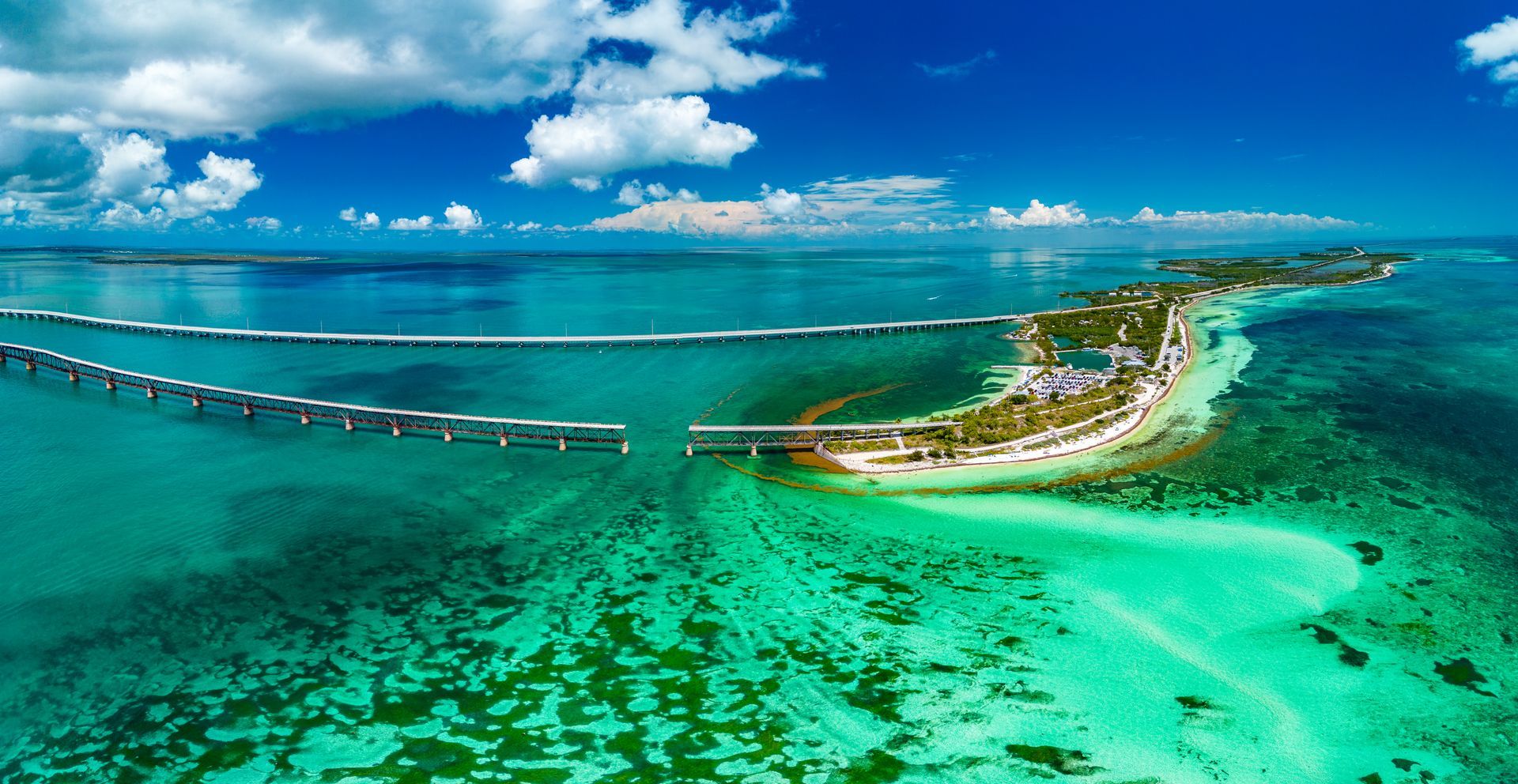 Aerial view: turquoise water, island, bridge, blue sky, white clouds.