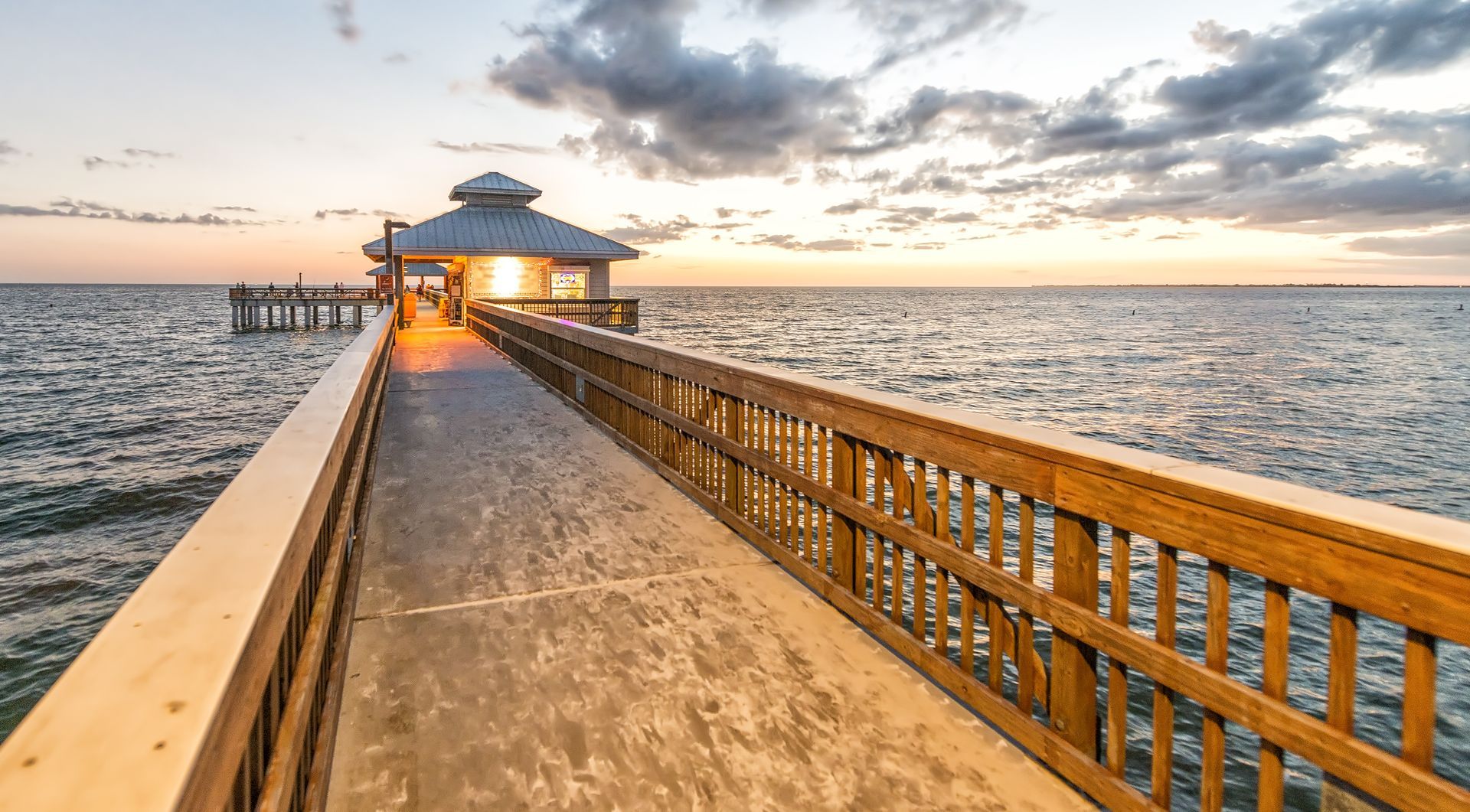 Wooden pier extending over calm water towards a gazebo at sunset.