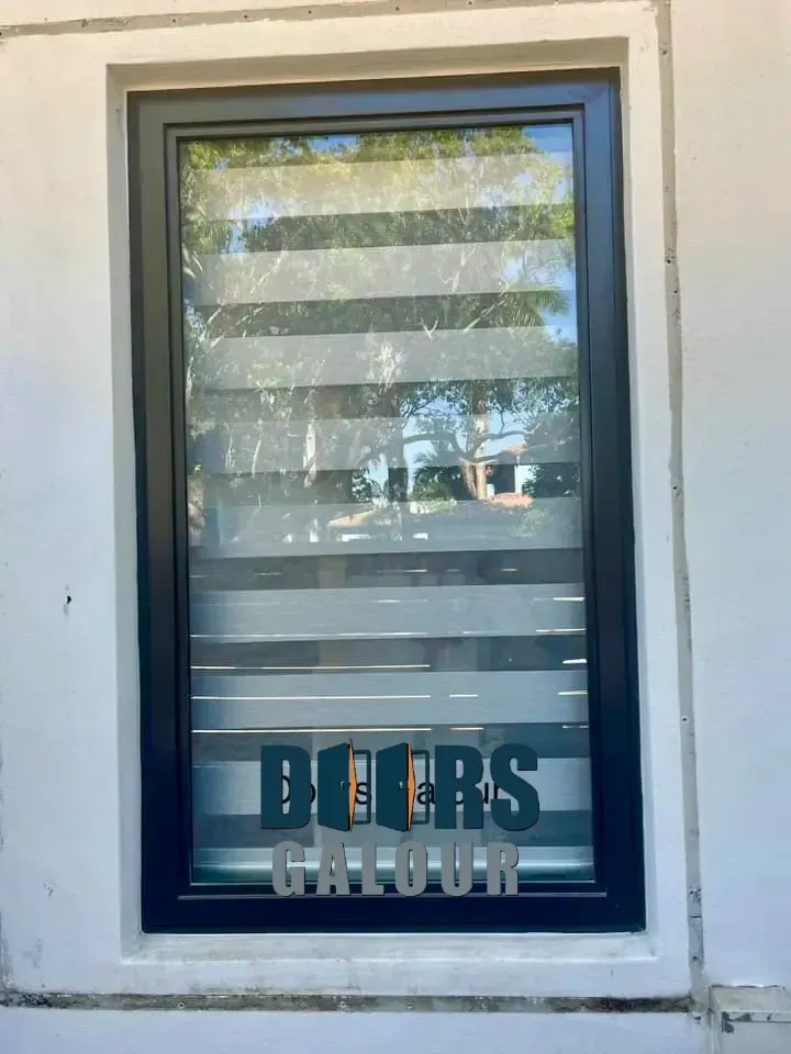 Three vertical windows with blue trim, reflecting a green yard, set in a wood-shingled wall.
