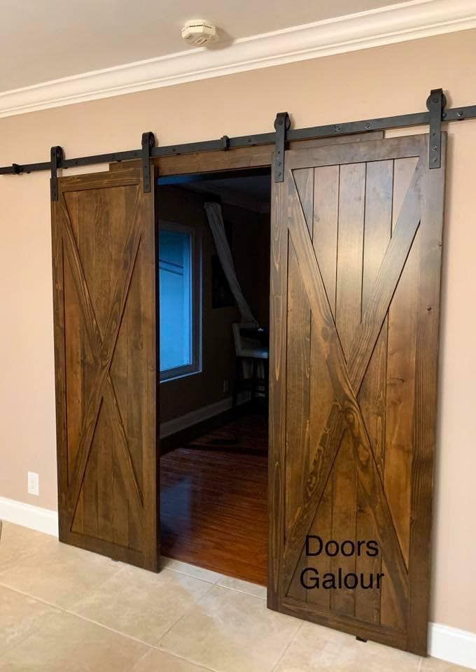 Barn-style double doors, stained dark brown, with black hardware, open to another room.