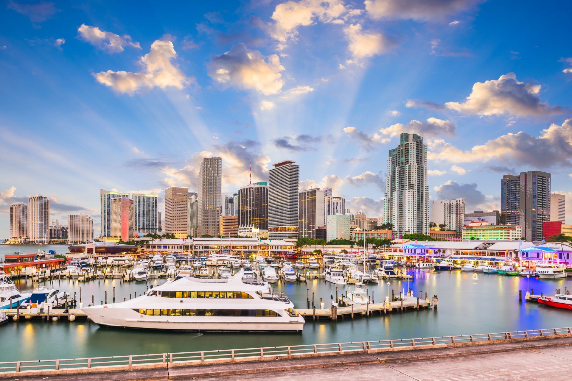 Miami skyline with yachts in a harbor, under a bright blue sky with clouds.