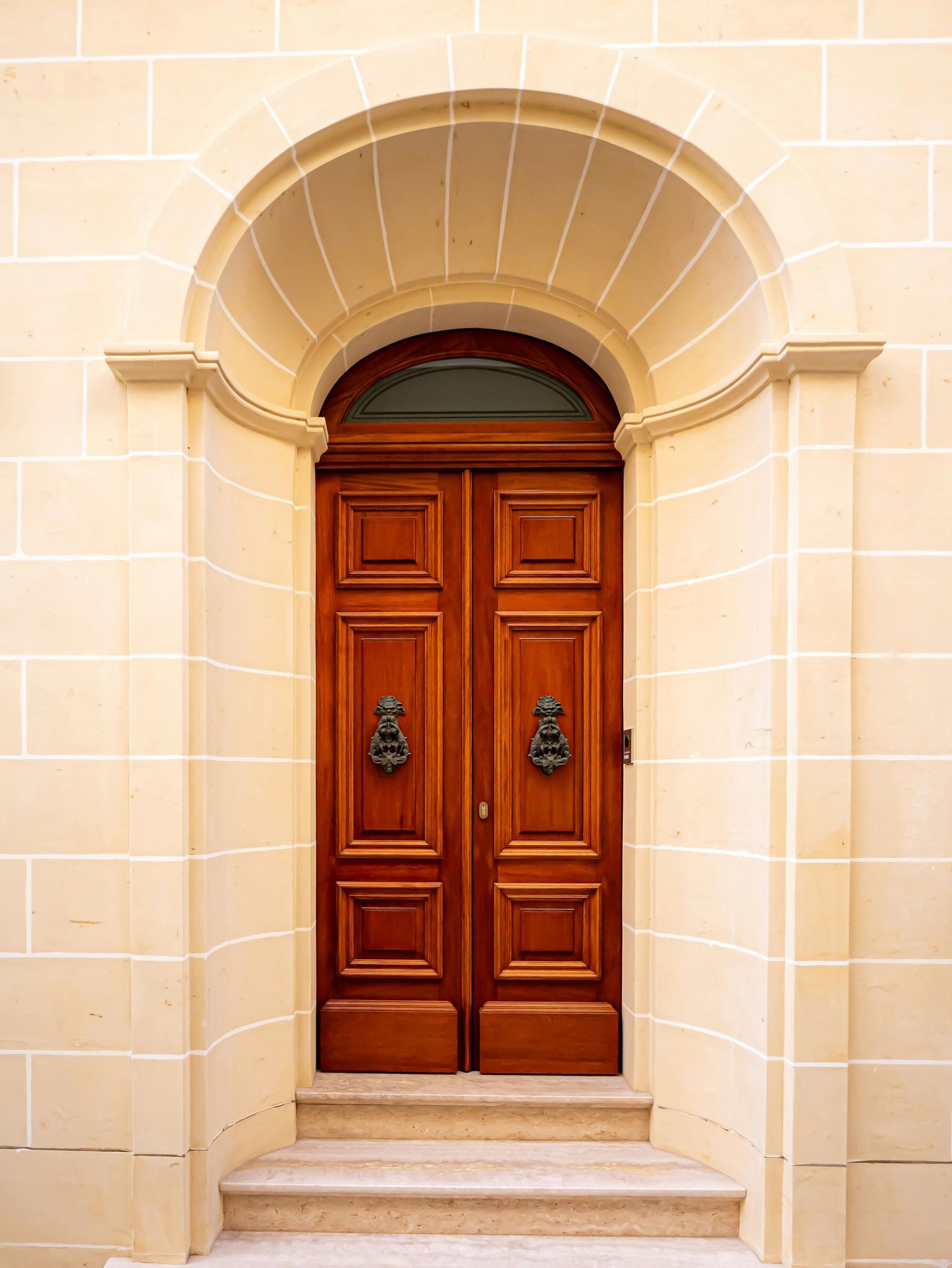 Old, weathered wooden door with rusted panels, shadowed by a tree. Situated in a stone wall.