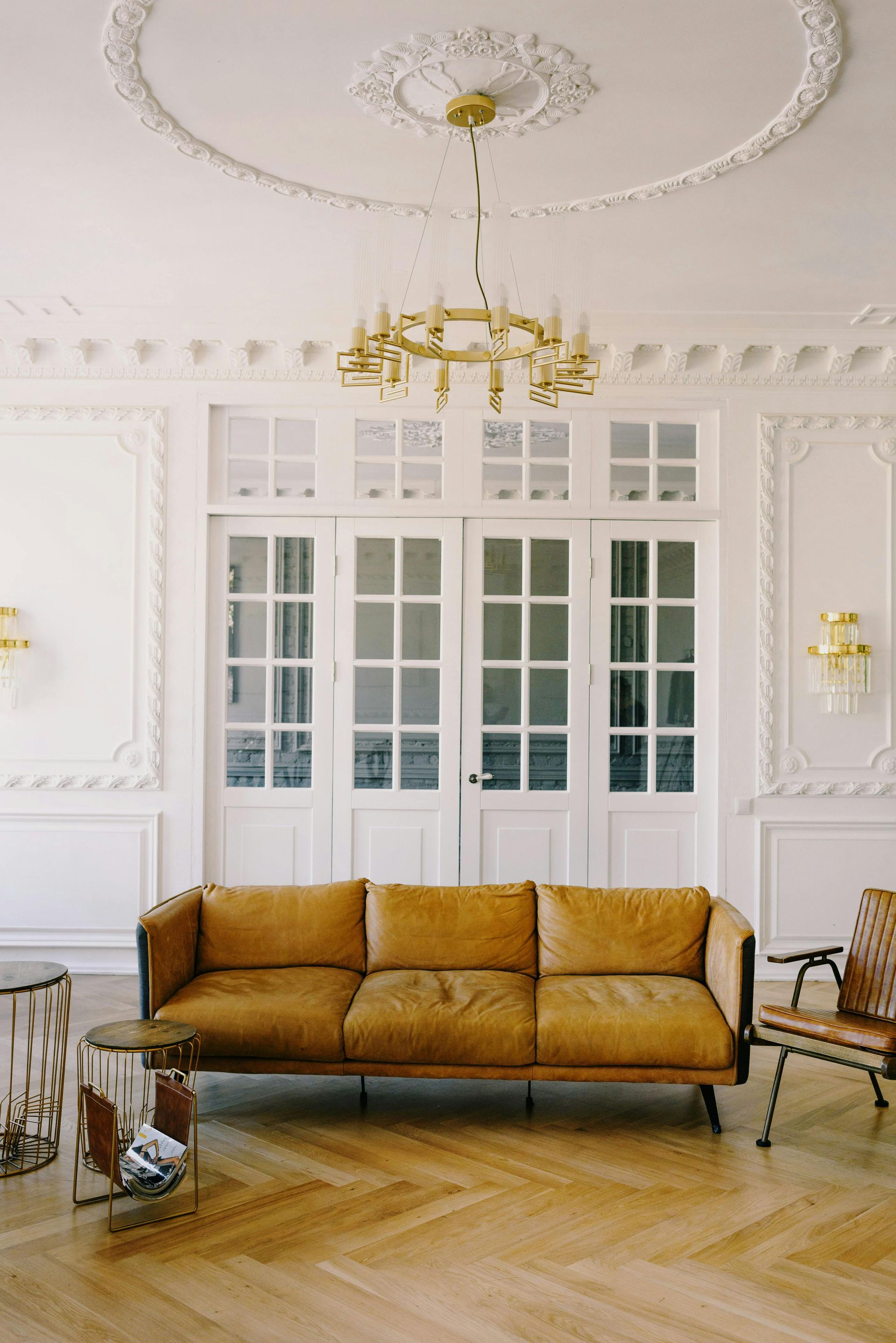 Elegant living room with tan leather sofa, gold chandelier, and ornate white molding.