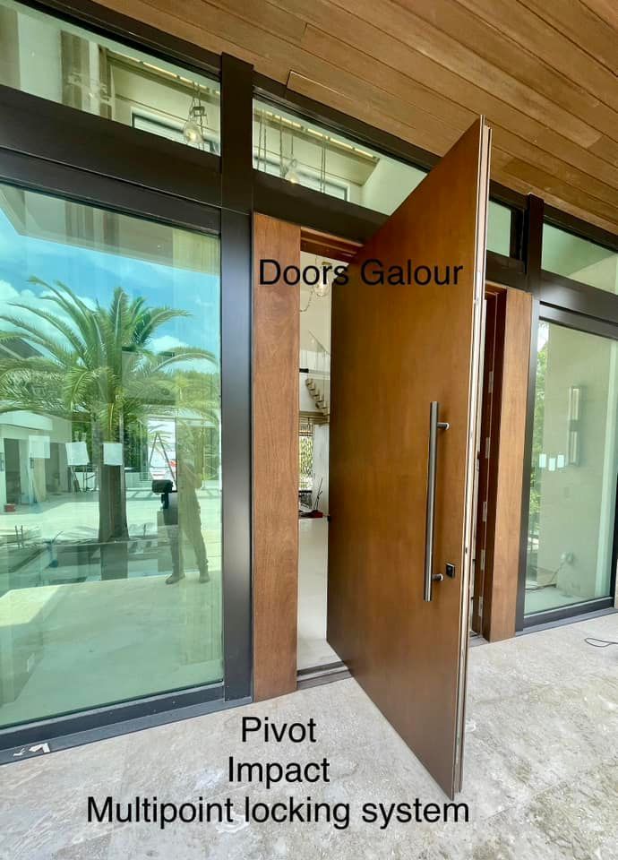 Large wooden pivot door with multipoint locking system; glass windows, palm tree visible.