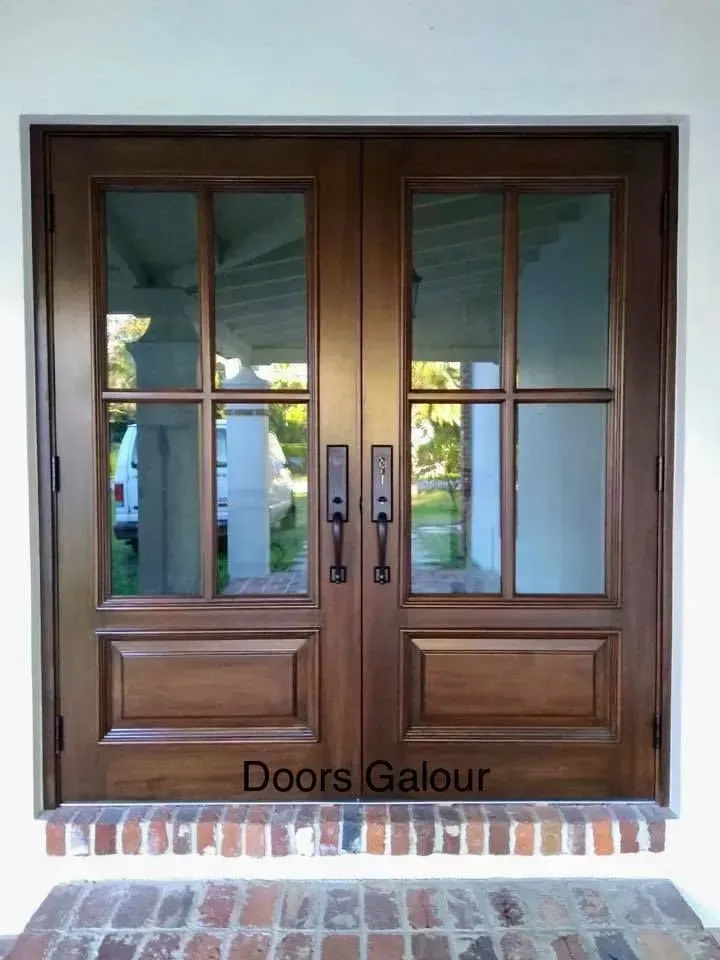 Wooden double doors with glass panels and black handles set in a white doorframe on a brick step.