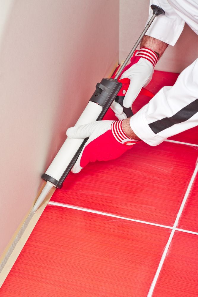 A Man Is Applying Sealant To A Red Tile Floor — Illawarra Fasteners Pty Ltd In Unanderra, NSW