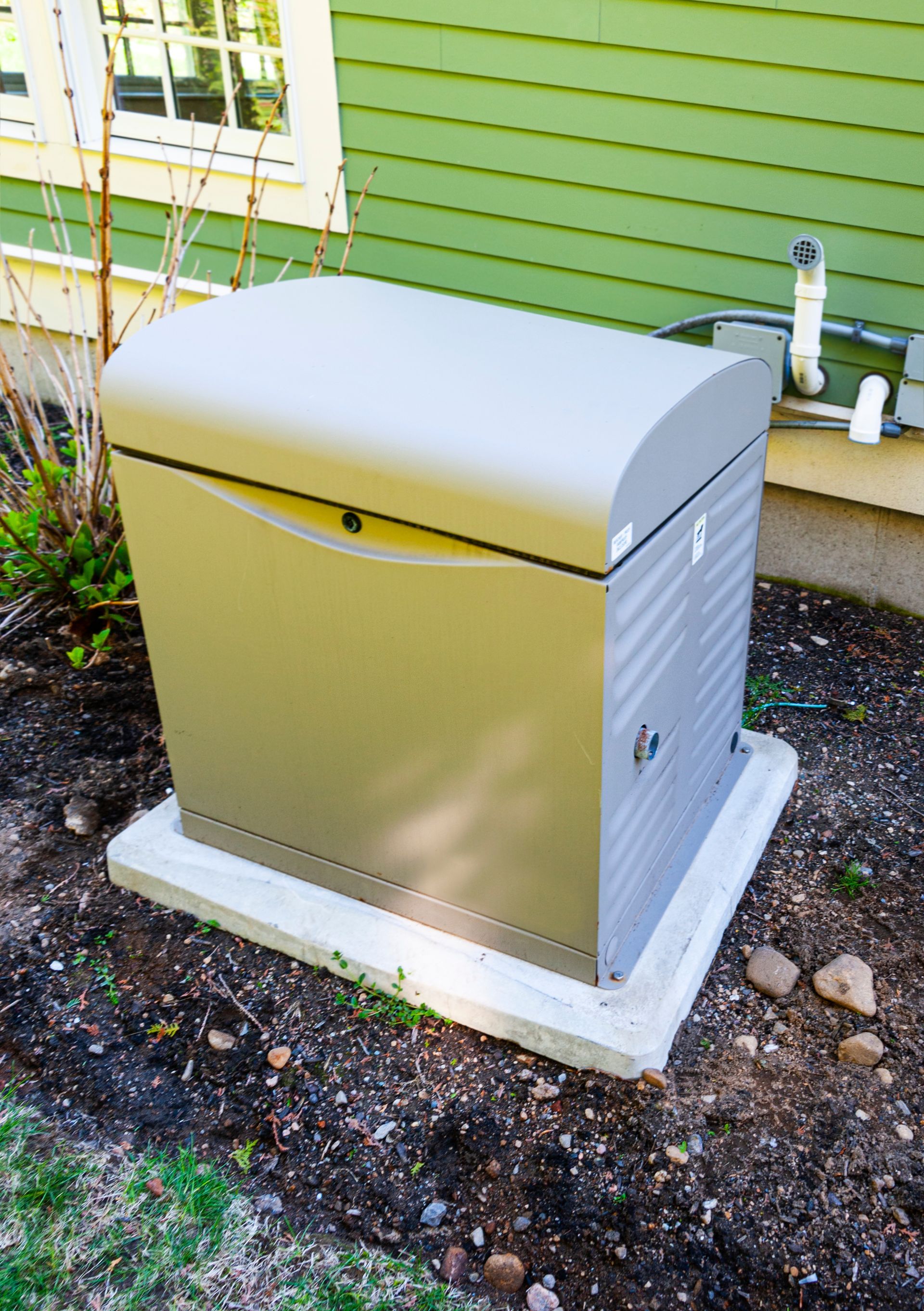 Beige outdoor utility box on a concrete pad beside a green house wall.